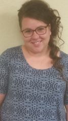 A woman wearing glasses and a blue shirt is smiling for the camera.