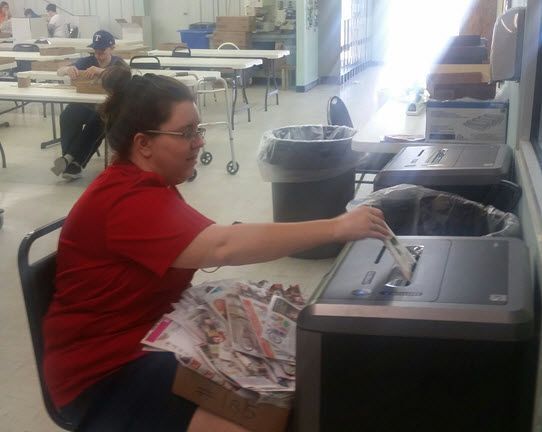 A woman in a red shirt is putting a piece of paper into a machine