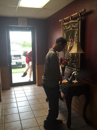 A man is standing in a hallway looking at a laptop.