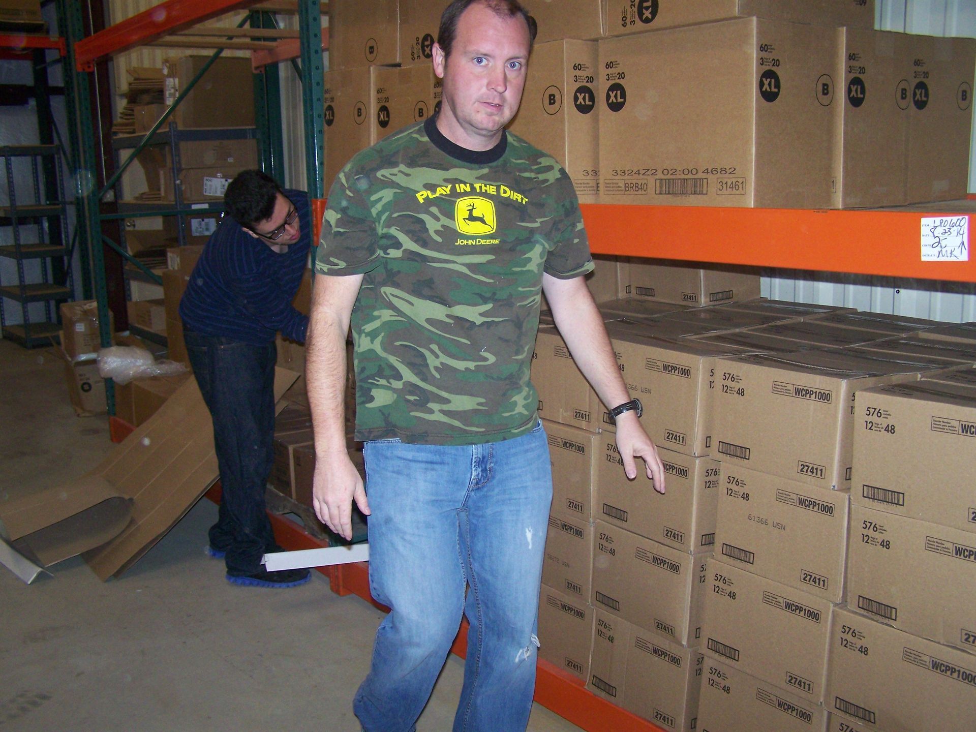 A man wearing a john deere shirt stands in a warehouse