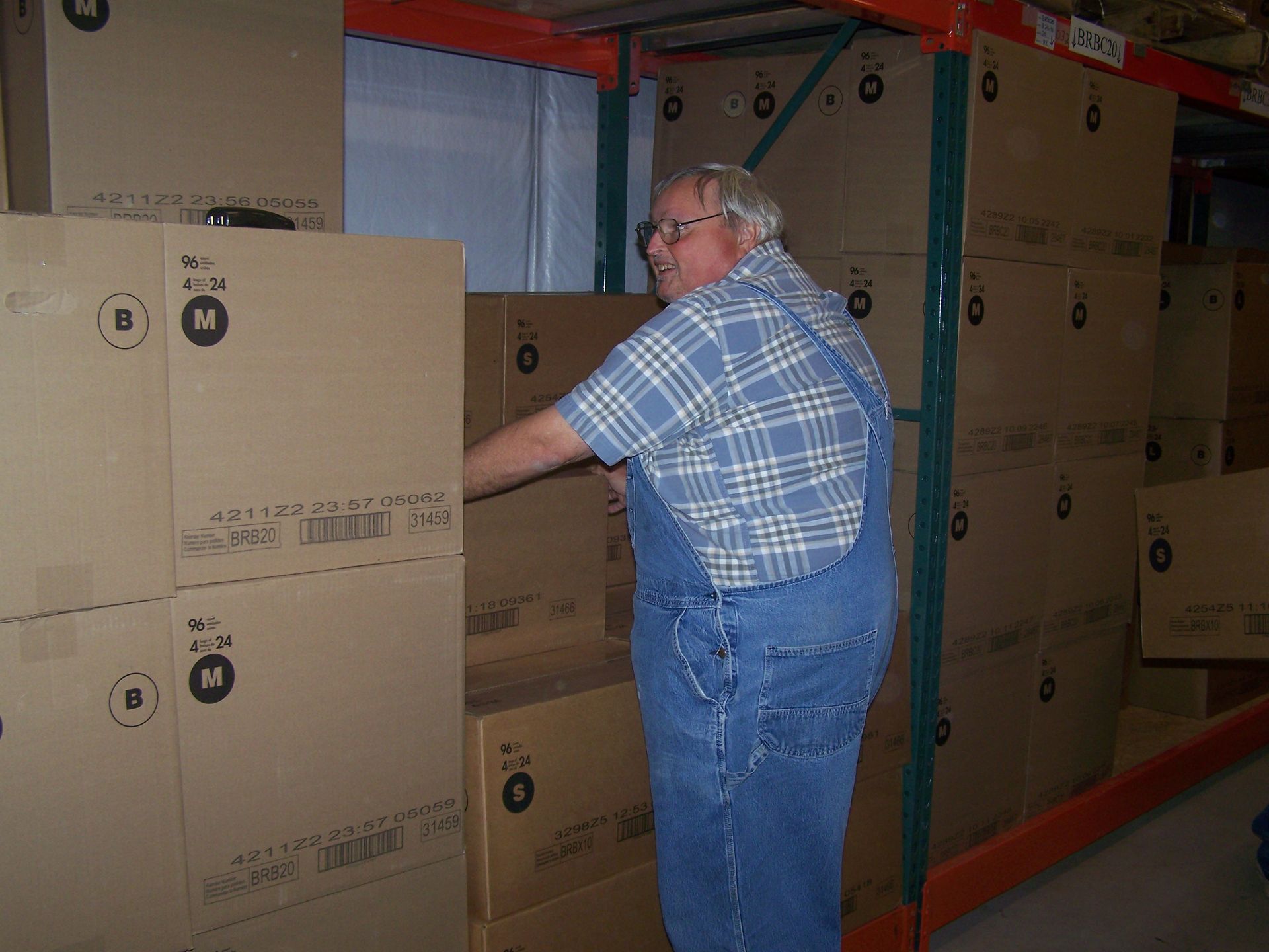 A man in overalls is reaching for a box in a warehouse