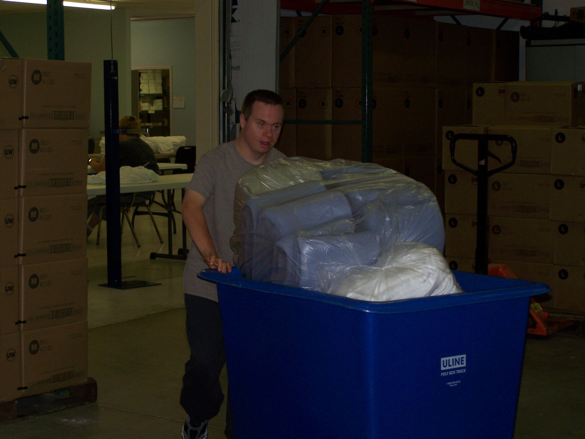 A man is pushing a large blue bin in a warehouse.
