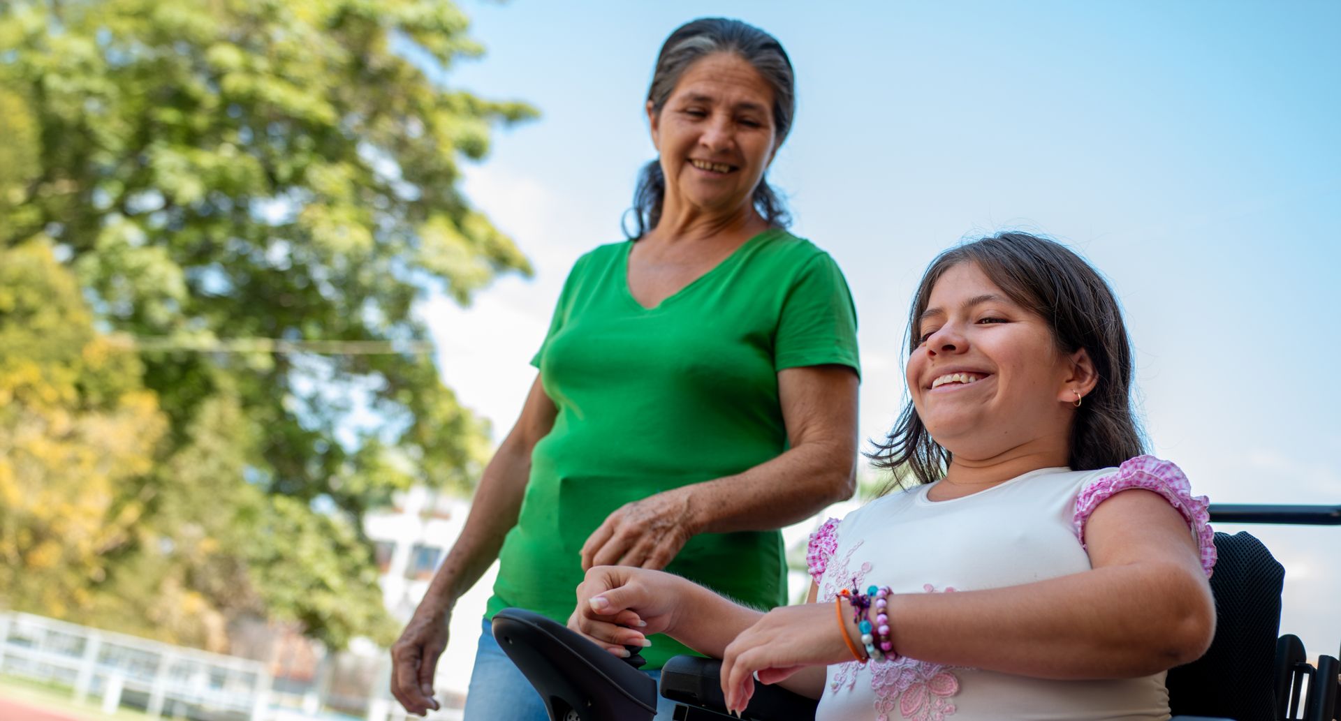 A woman is standing next to a girl in a wheelchair.