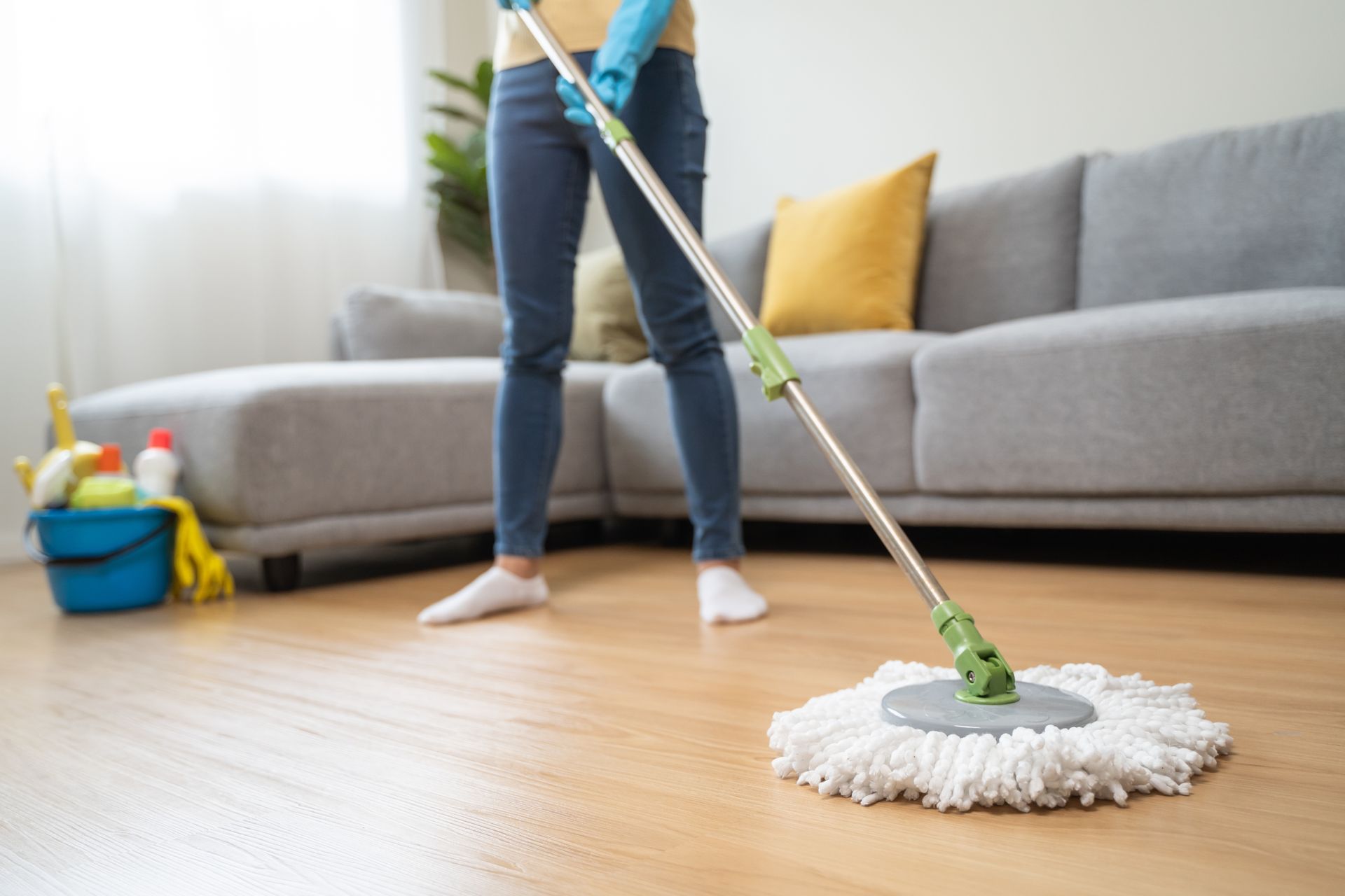 A woman is cleaning the floor in a living room with a mop.