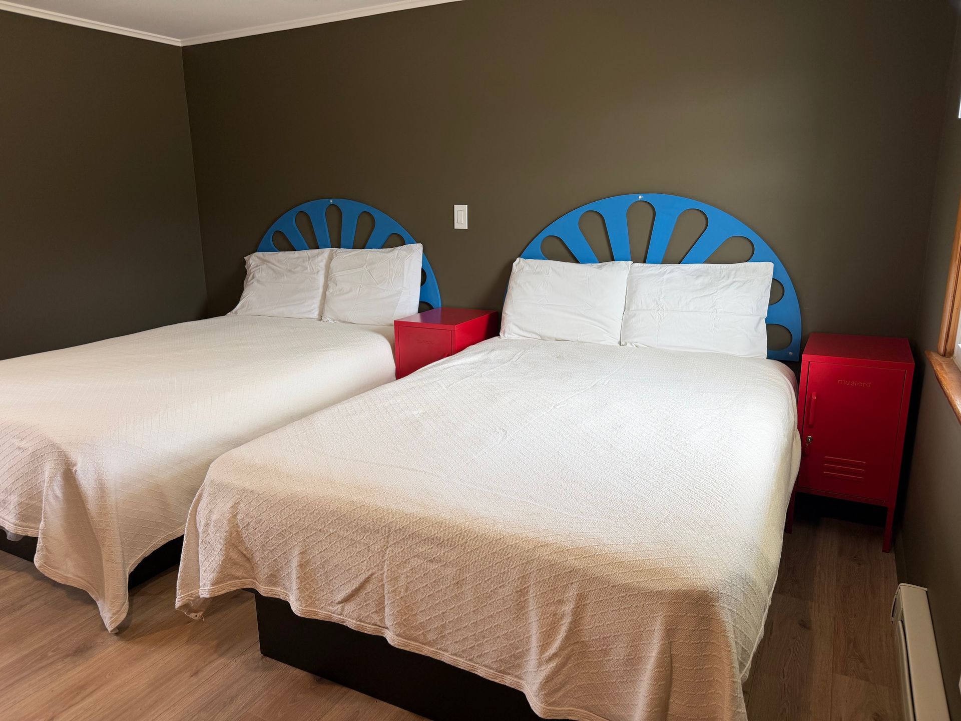 Two twin beds with white bedding and blue headboards in a simple bedroom with red nightstands.
