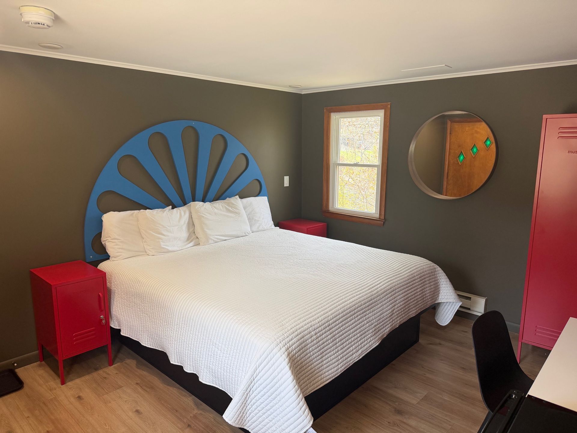 Modern bedroom with white bed, blue sunburst headboard, red nightstands, and gray walls