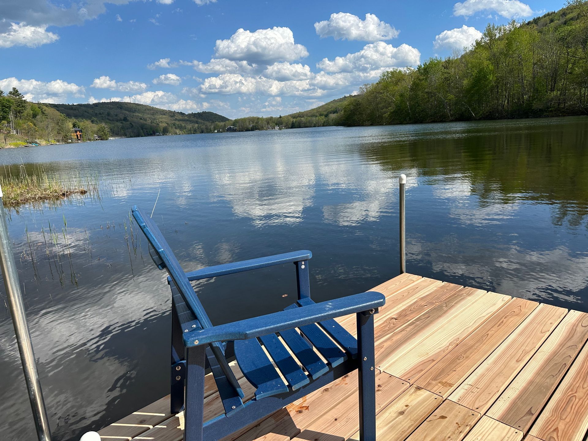 Blue chair on a wooden dock overlooking a calm lake and forested hills under a partly cloudy sky