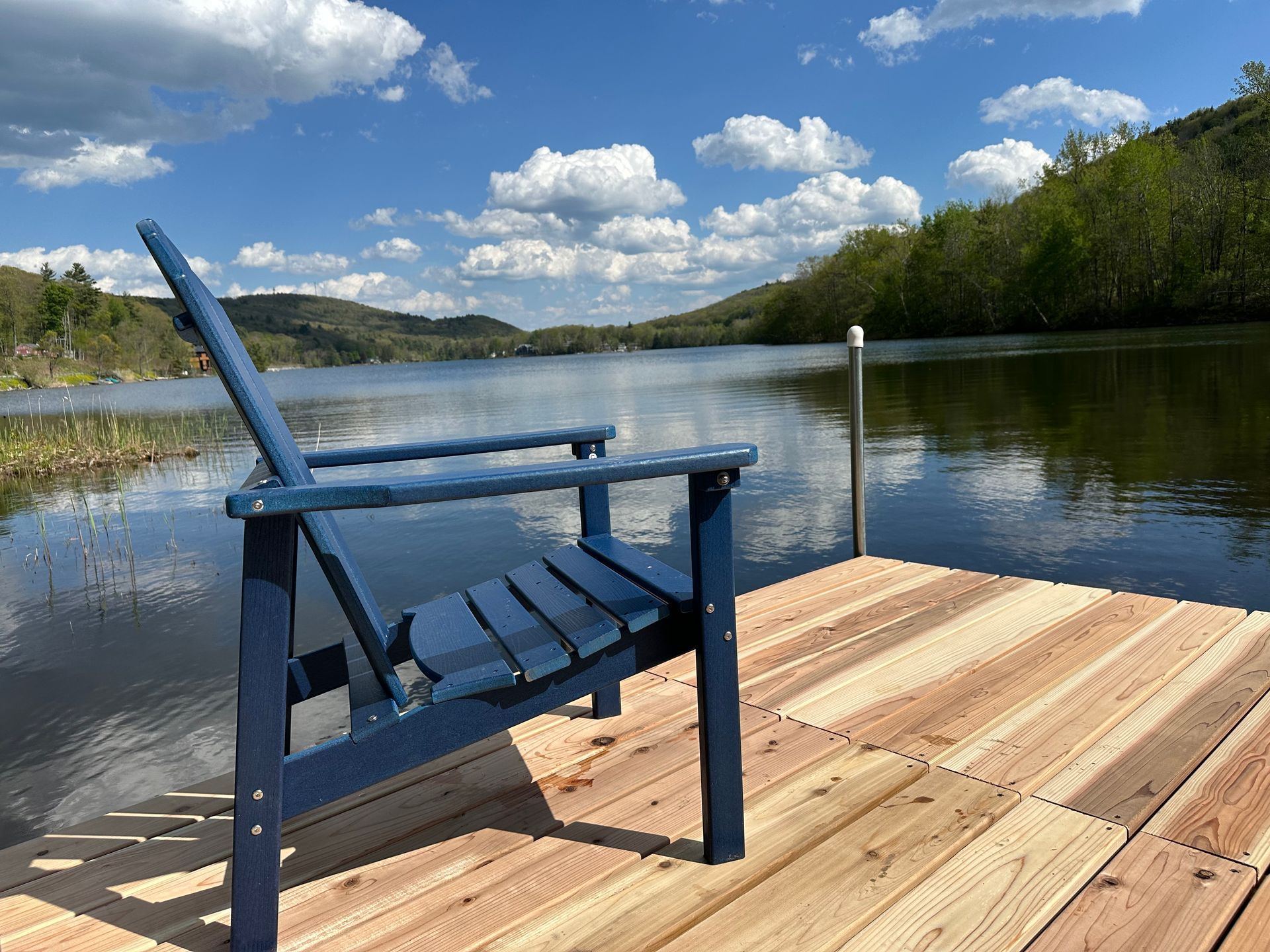 Blue chair on a wooden dock by a calm lake under a cloudy blue sky.