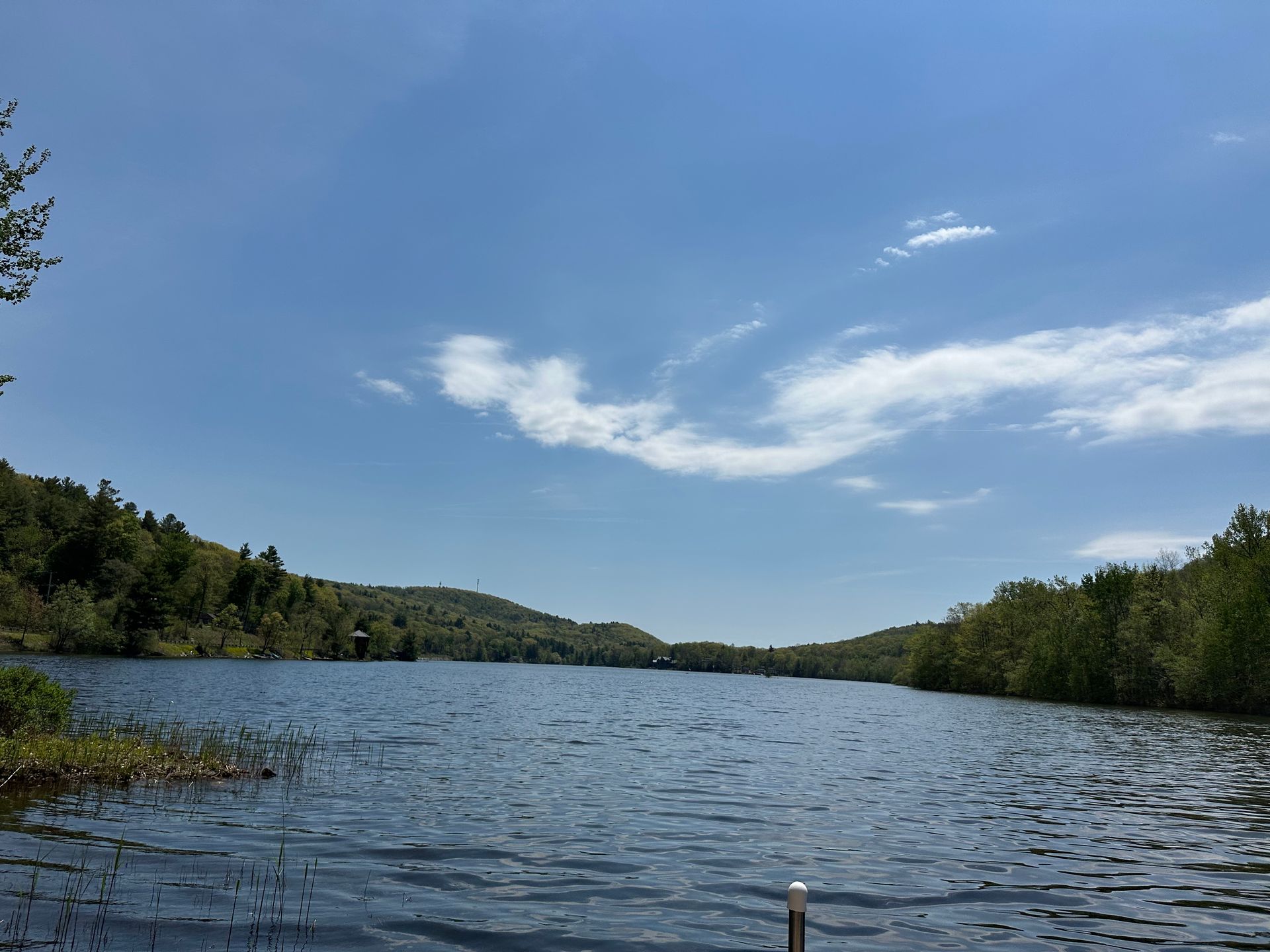 Calm lake with rippling water, green tree-lined shores, and a blue sky with wispy clouds