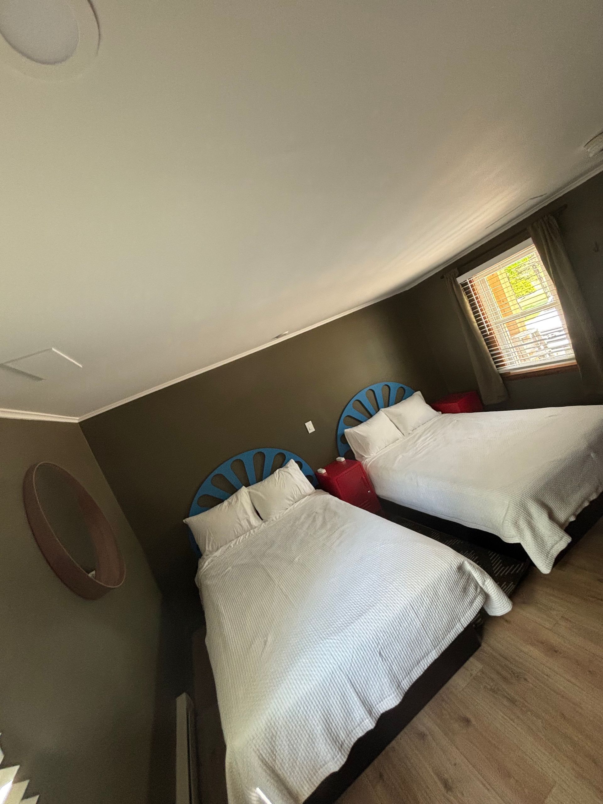 Bedroom with two twin beds dressed in white quilts, blue headboards, and a small window on the right.
