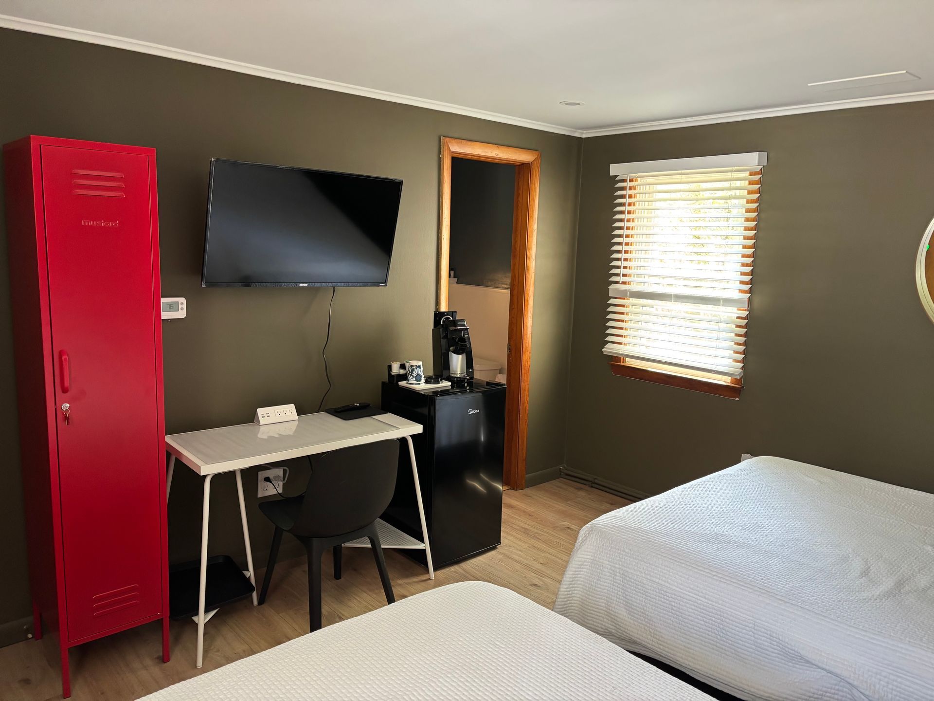 Small bedroom with a bed, desk, wall-mounted TV, red cabinet, and window blinds