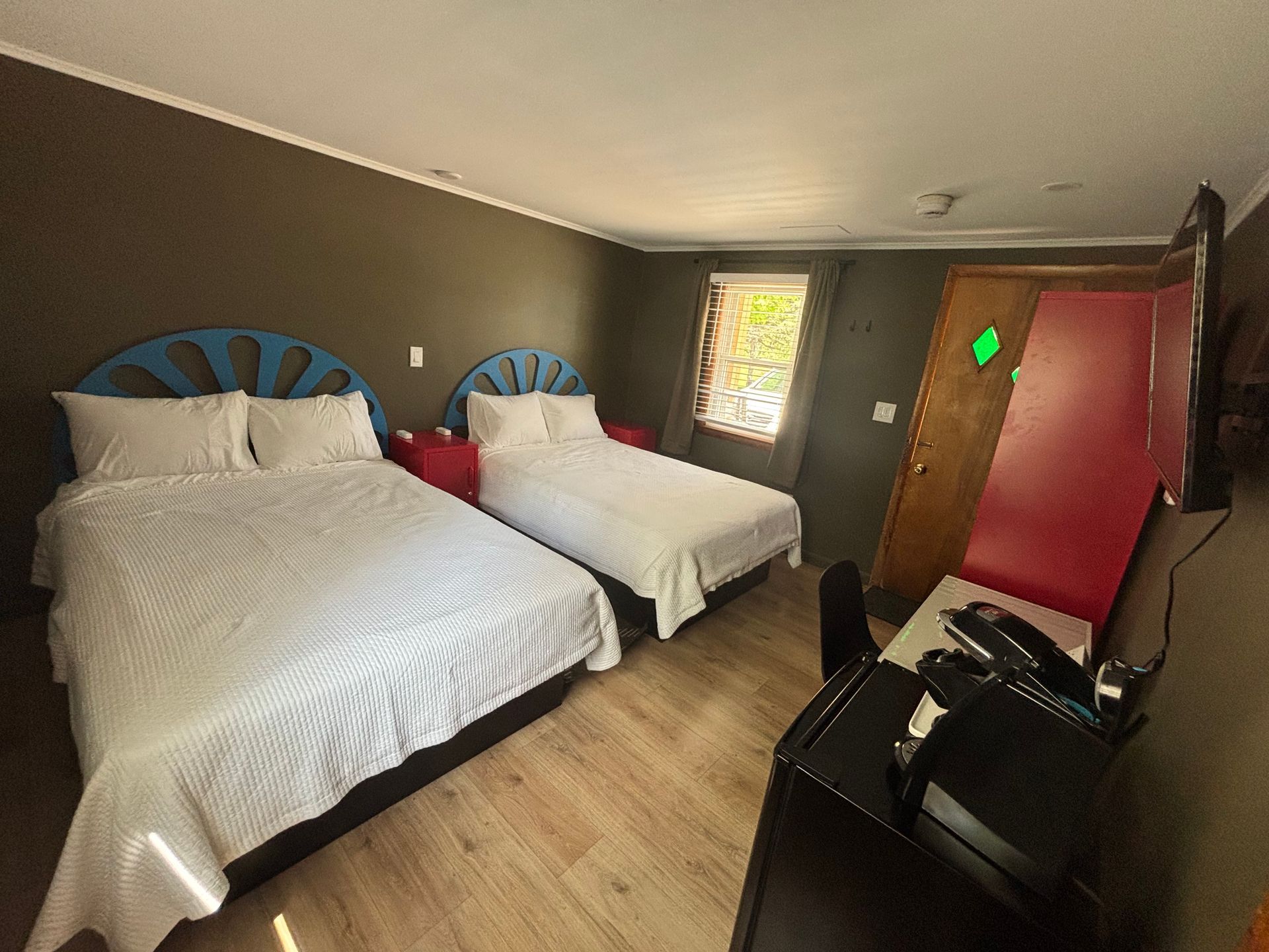 Hotel room with two white beds, blue headboards, wood floor, and a red door.