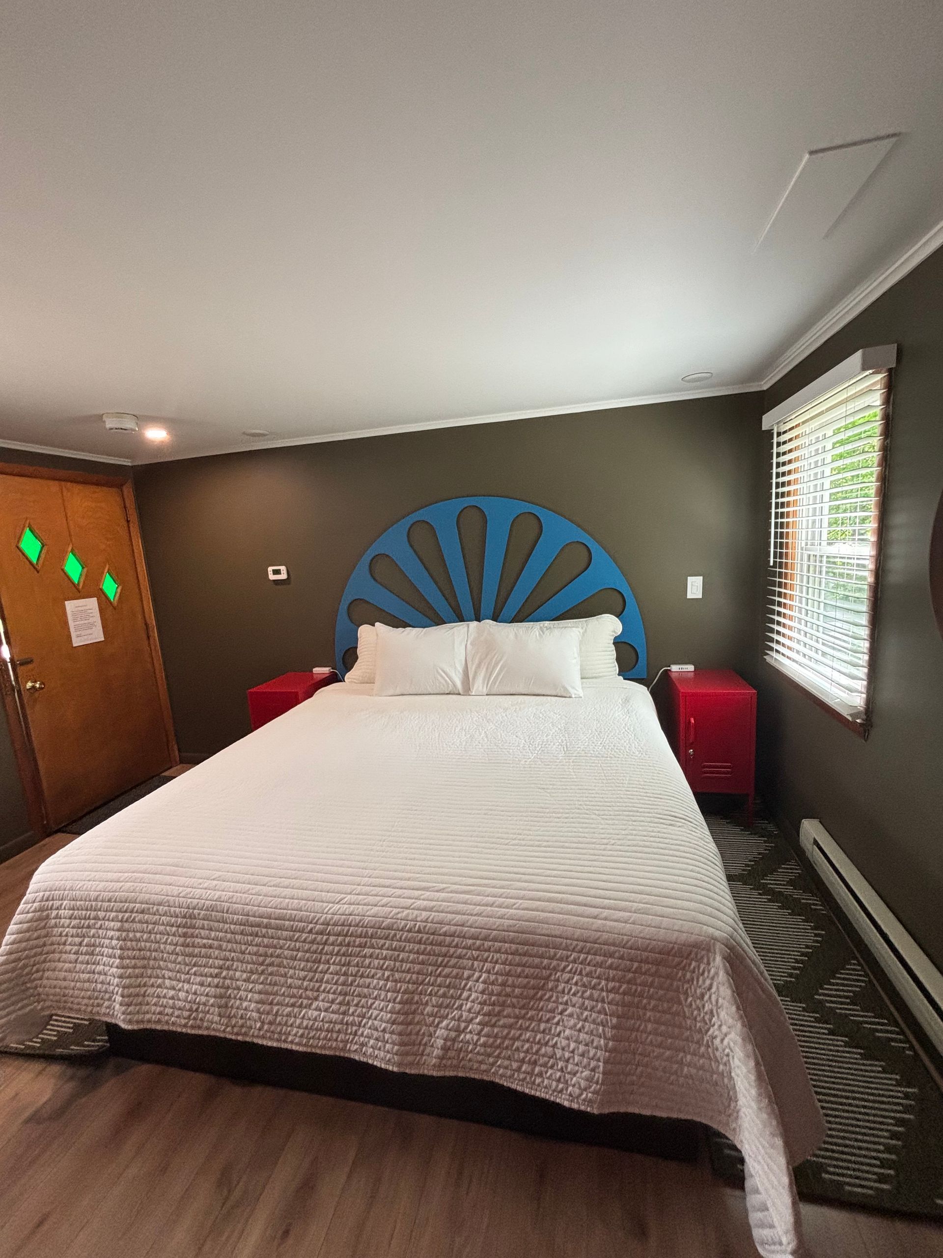 Bedroom with white bedspread, blue headboard, red chairs, and window blinds on the right