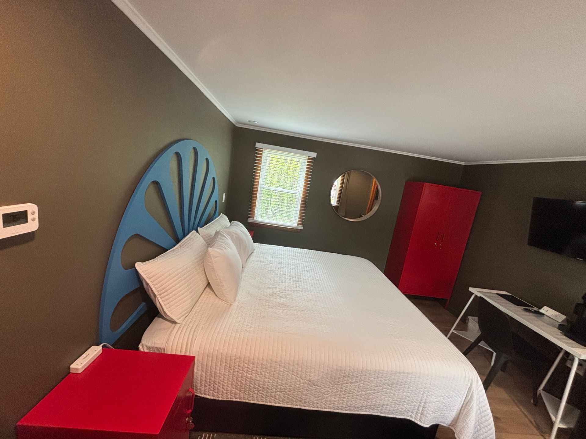 Modern bedroom with a bed, blue shell headboard, red side table, and wall-mounted TV