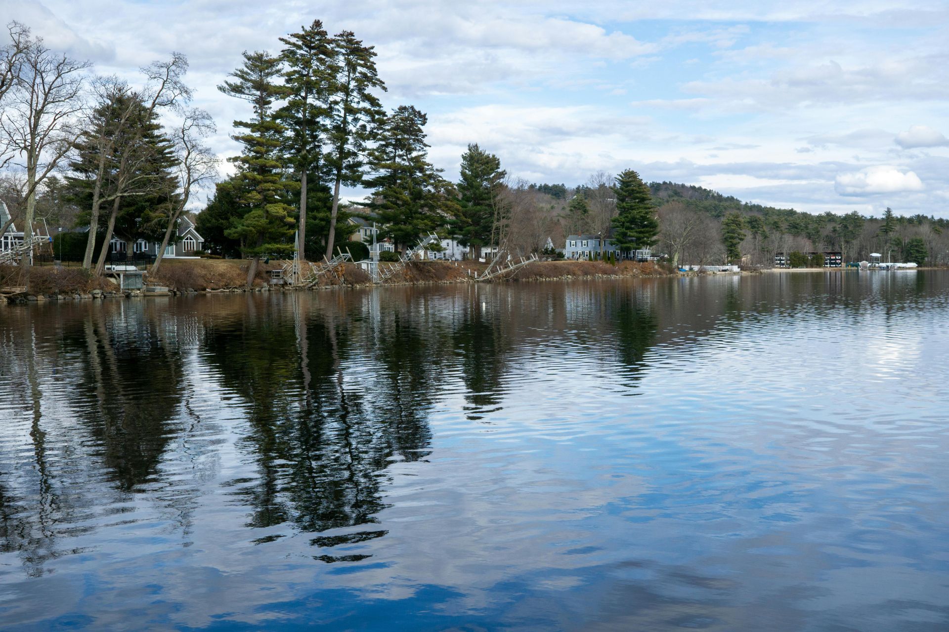 Calm lake reflecting trees and cloudy sky, with a wooded shoreline in the background