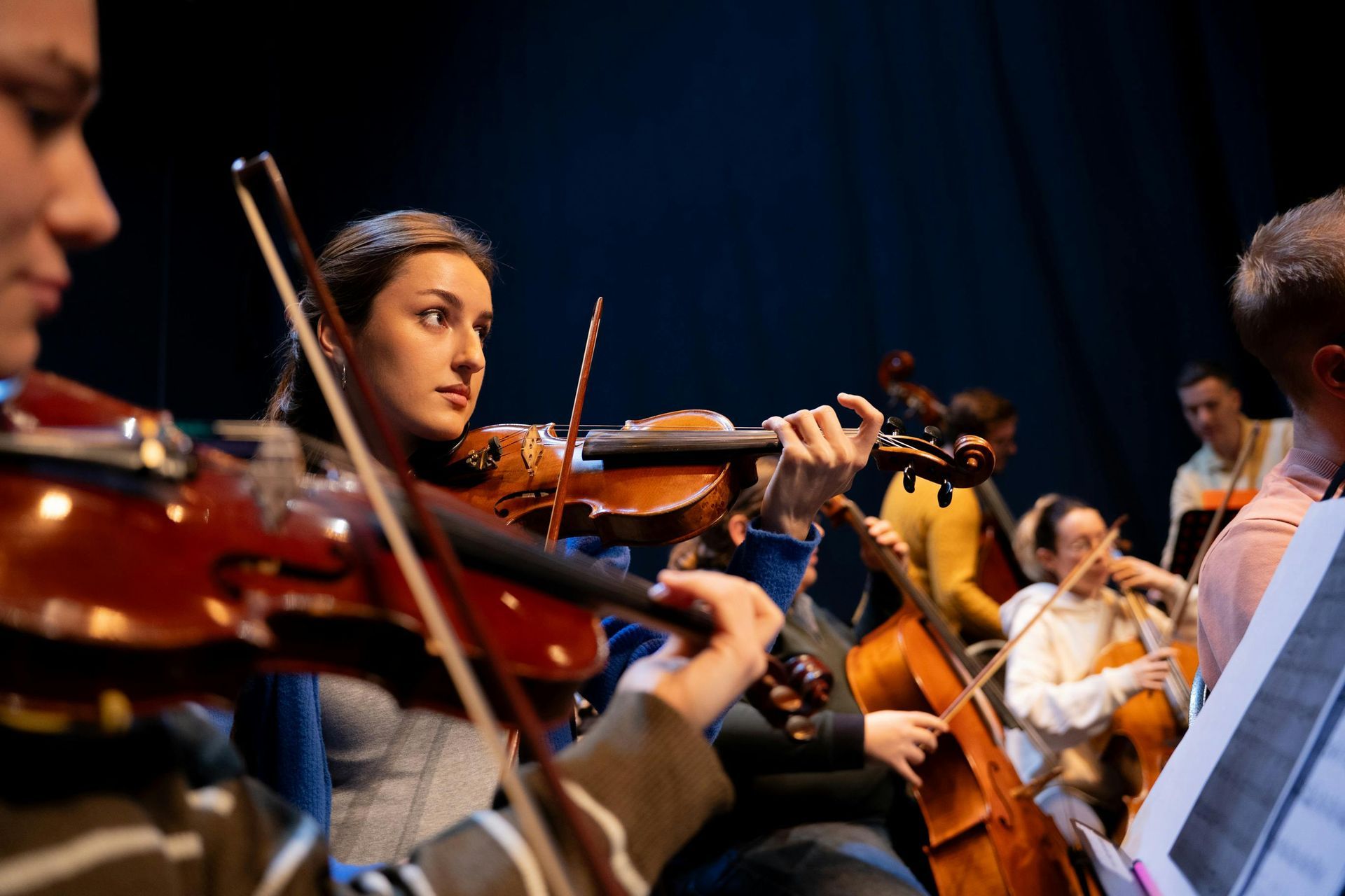 String musicians performing on stage under warm lights, with violins and sheet music stands.