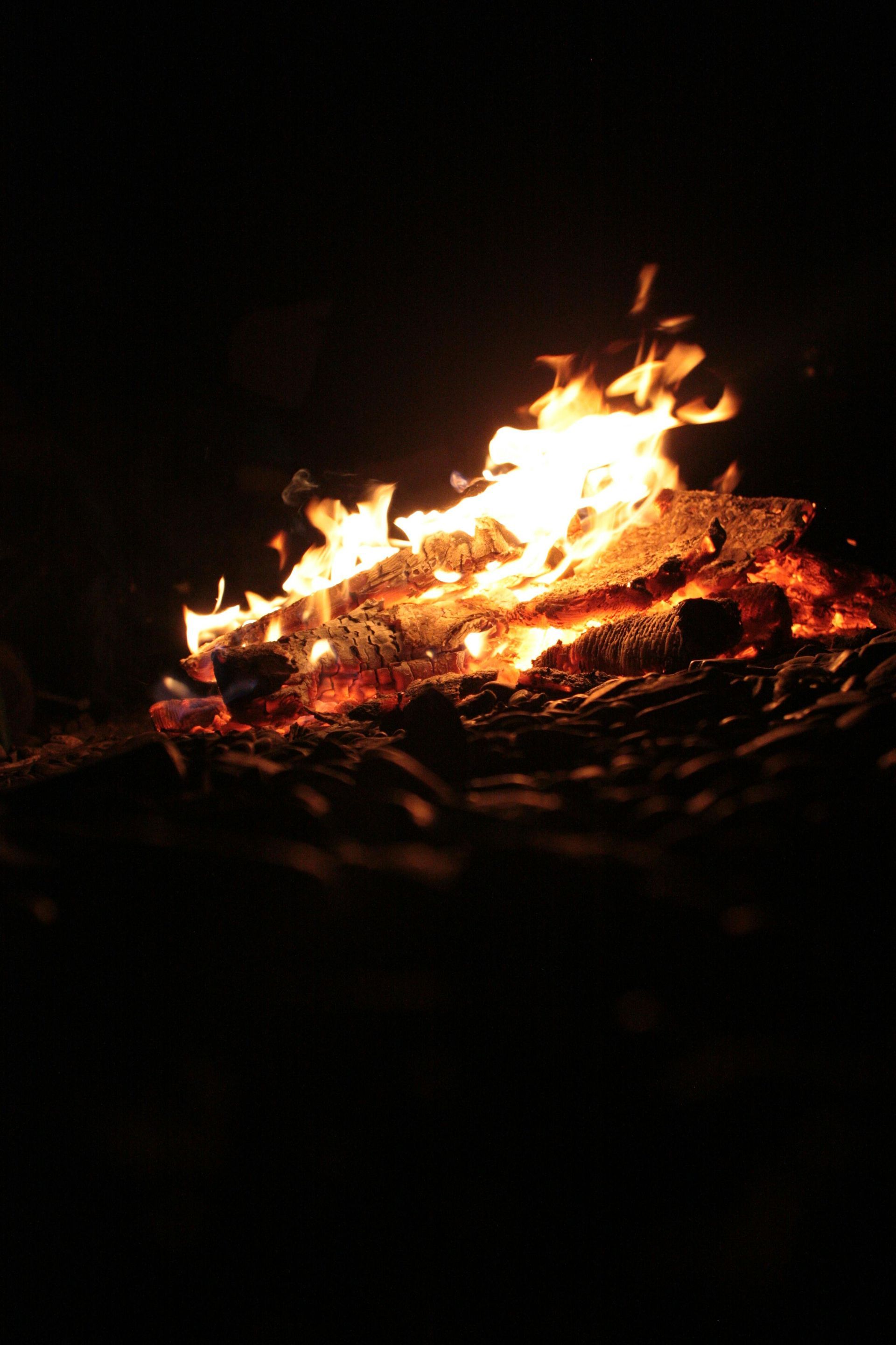 A small campfire burns on the ground, with bright orange flames against a dark night background.