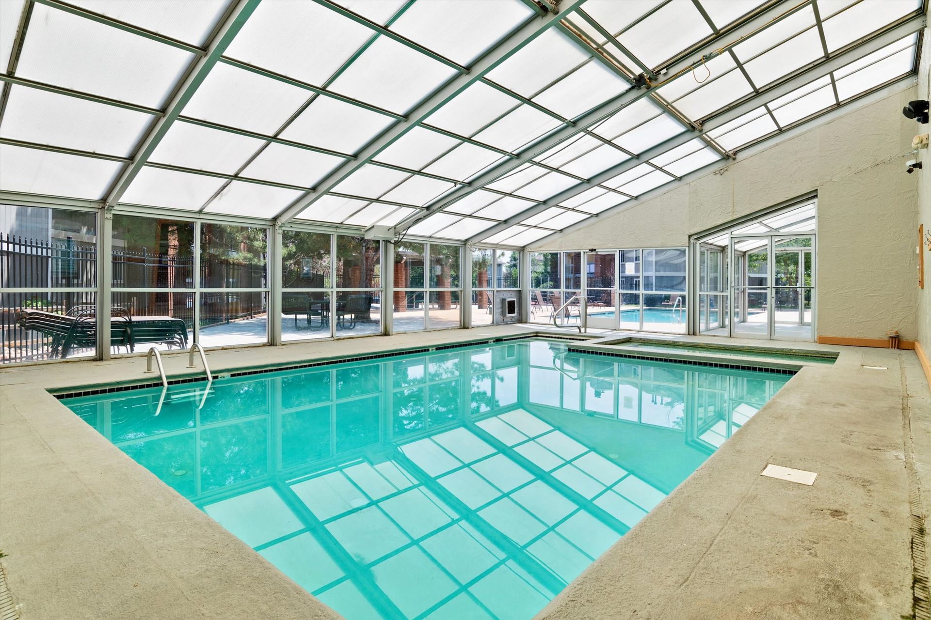 Indoor swimming pool with clear roof and walls, filled with turquoise water.