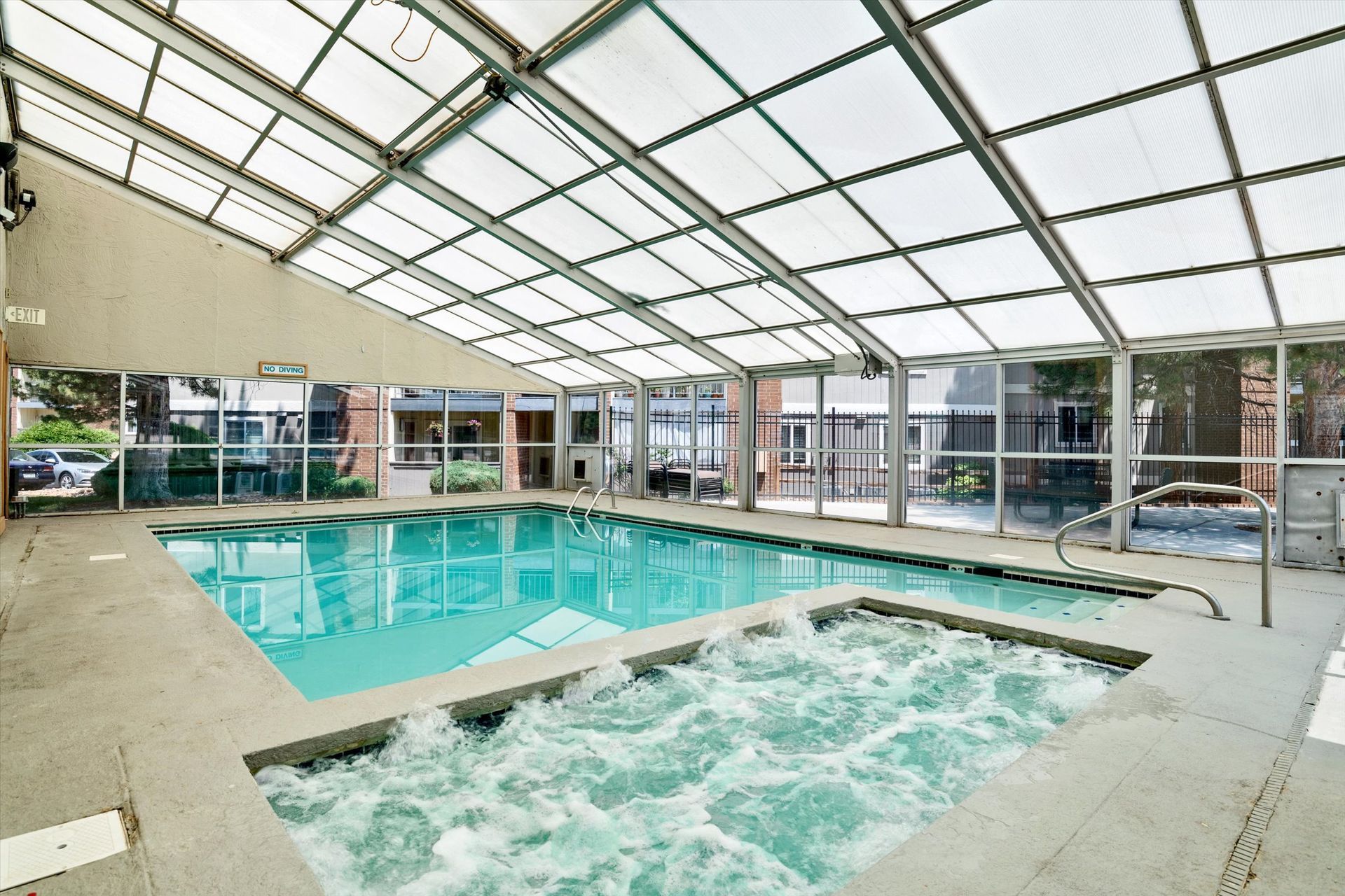 Indoor swimming pool and hot tub under a glass roof. The water is blue.