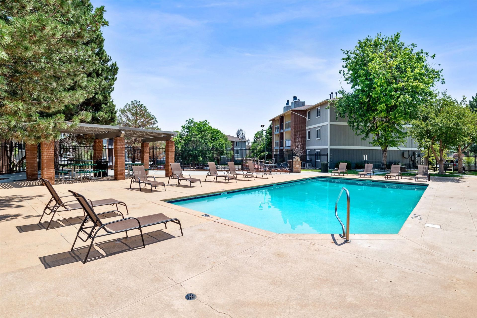 Pool area with lounge chairs, trees, and apartment buildings.