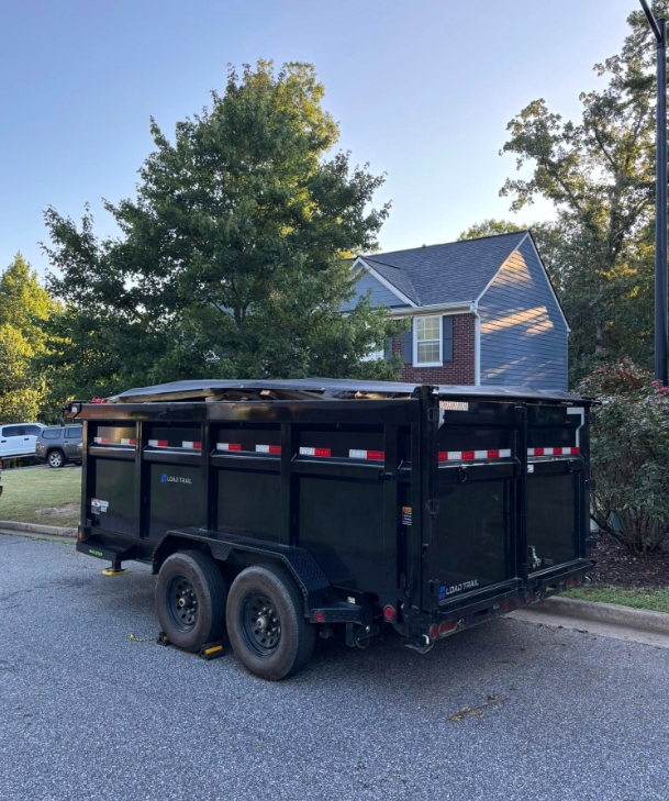 Orange dumpster truck parked on a street, next to a house.