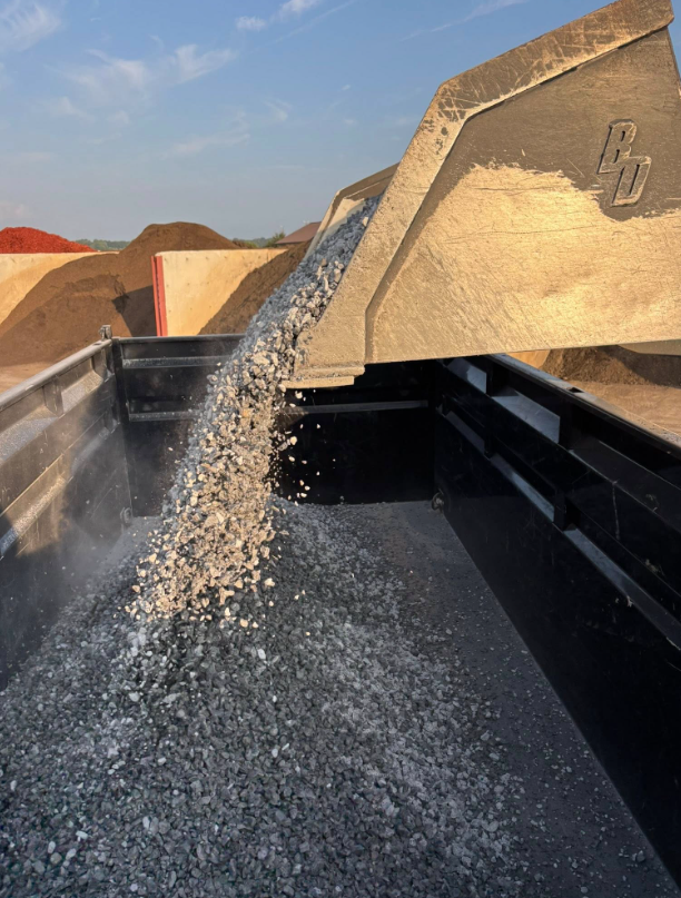 A front-end loader emptying gravel into a black truck bed, outdoors.