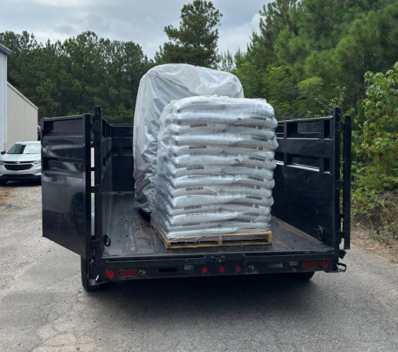 A flatbed trailer with bags of material on a pallet and a covered item, outside a building.