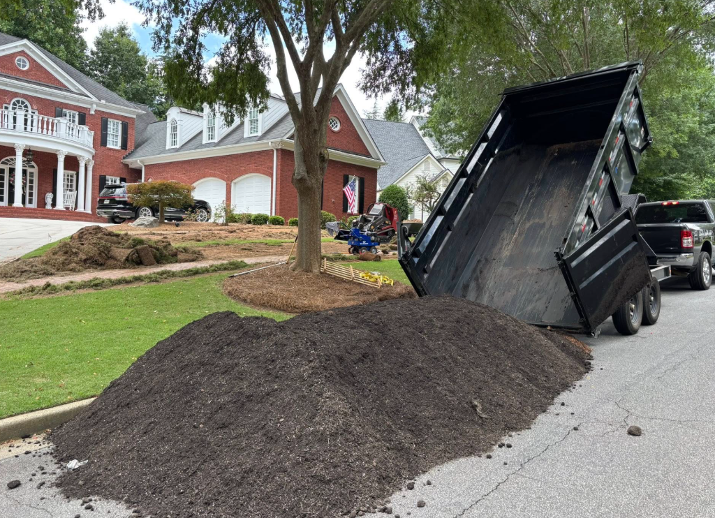 A dump truck unloading mulch onto a street in front of a house.