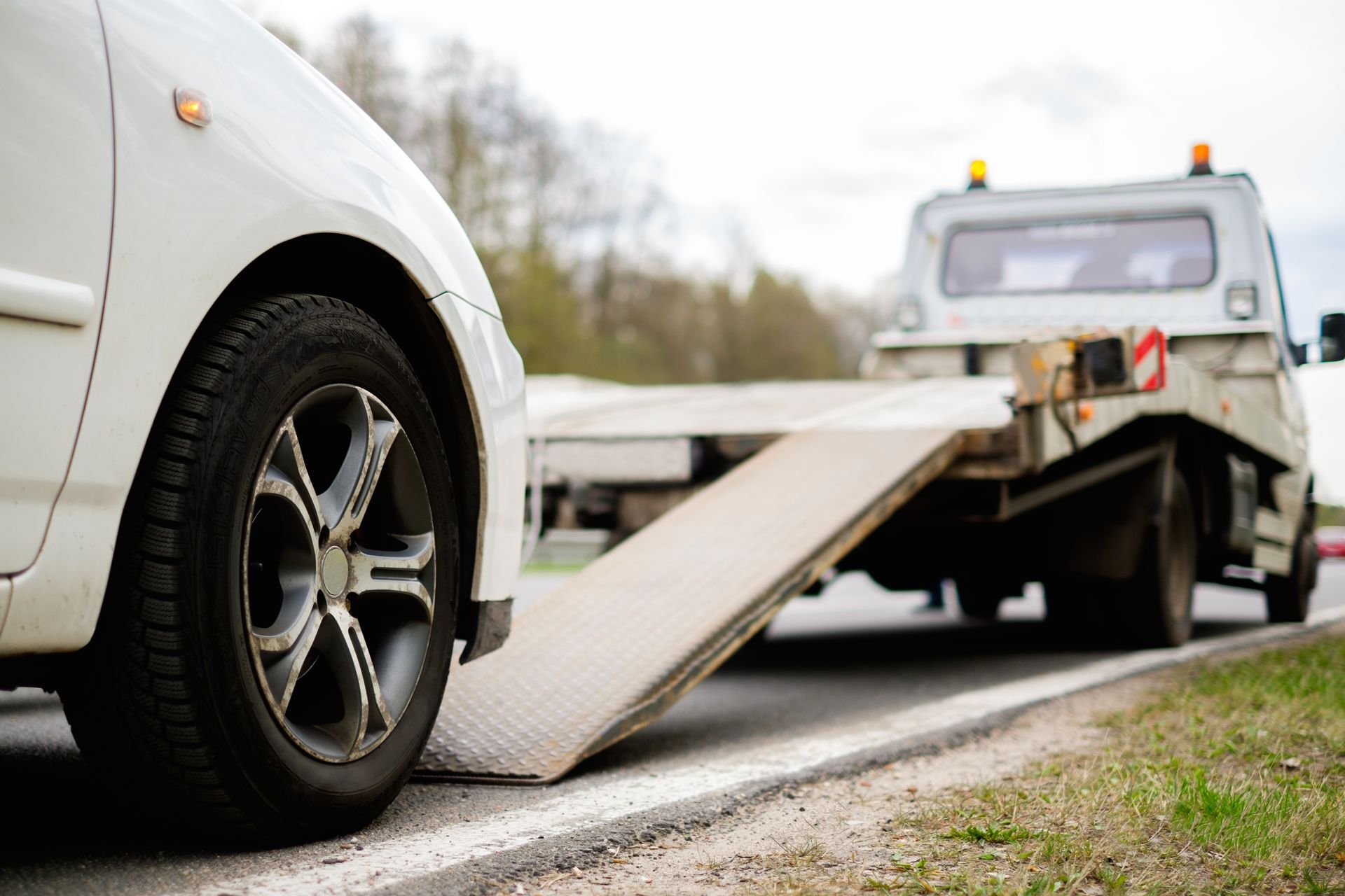 A white car is being towed by a tow truck on the side of the road.