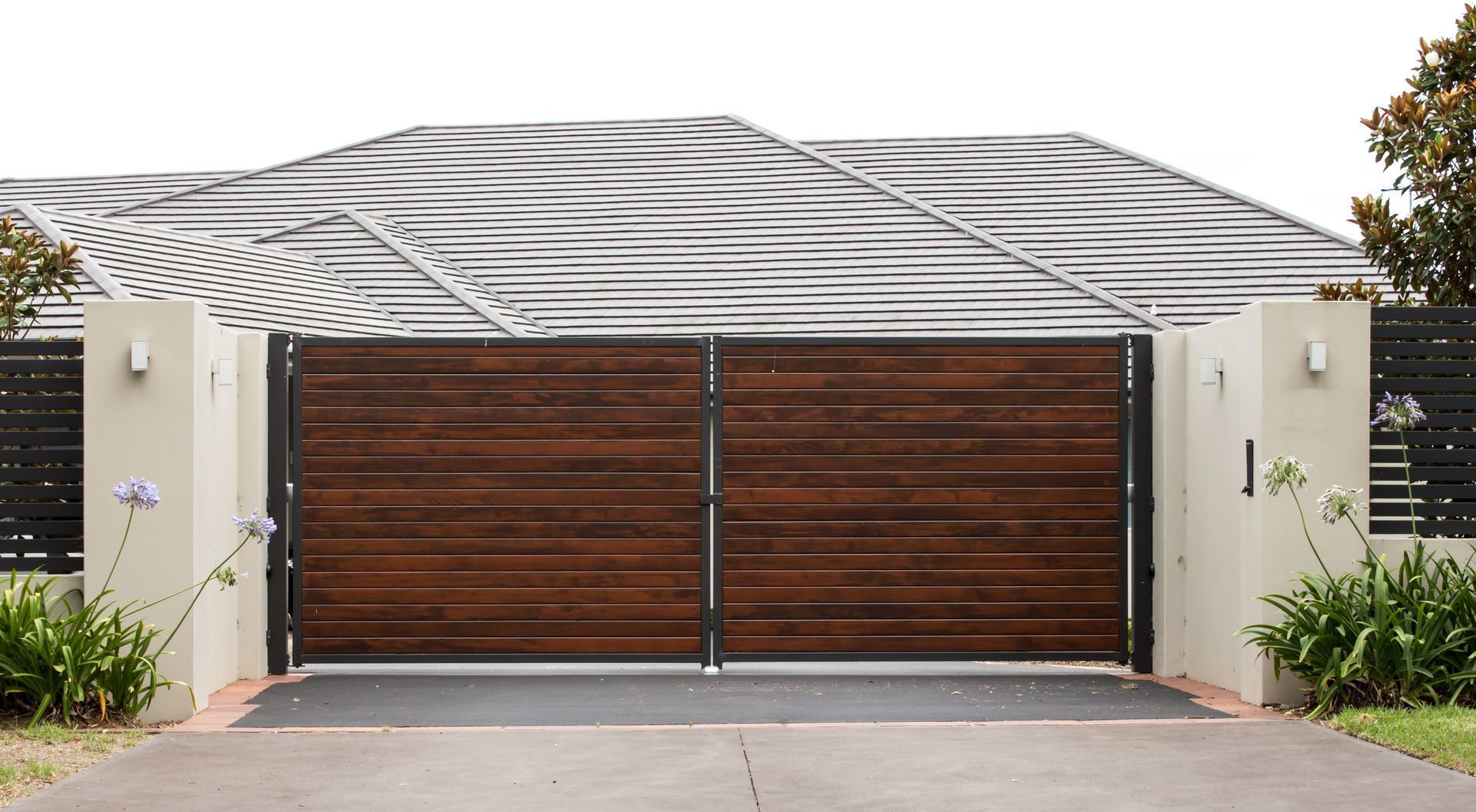 Wooden double driveway gates, dark brown, with light cream pillars, beneath a striped canopy.