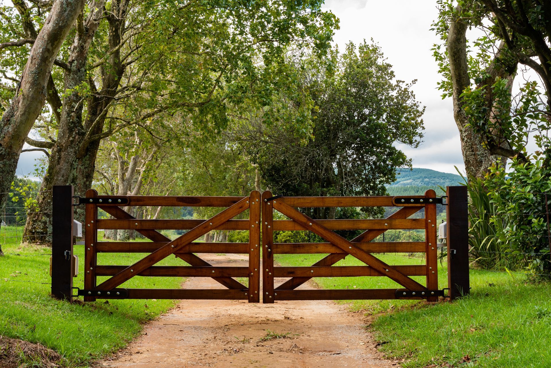 Wooden double gate with diagonal braces and metal hardware, set between brick and wooden fence.
