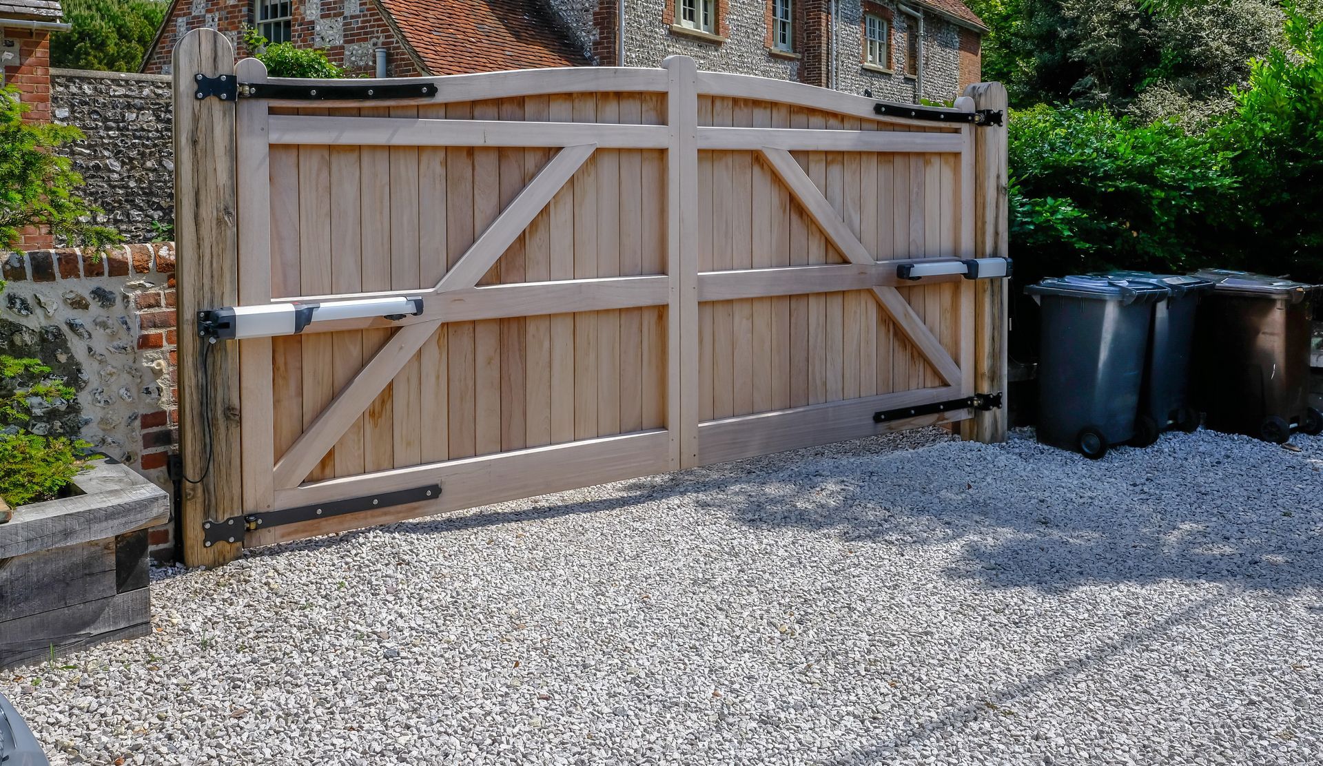 Wooden double driveway gates, light brown, set in gravel.