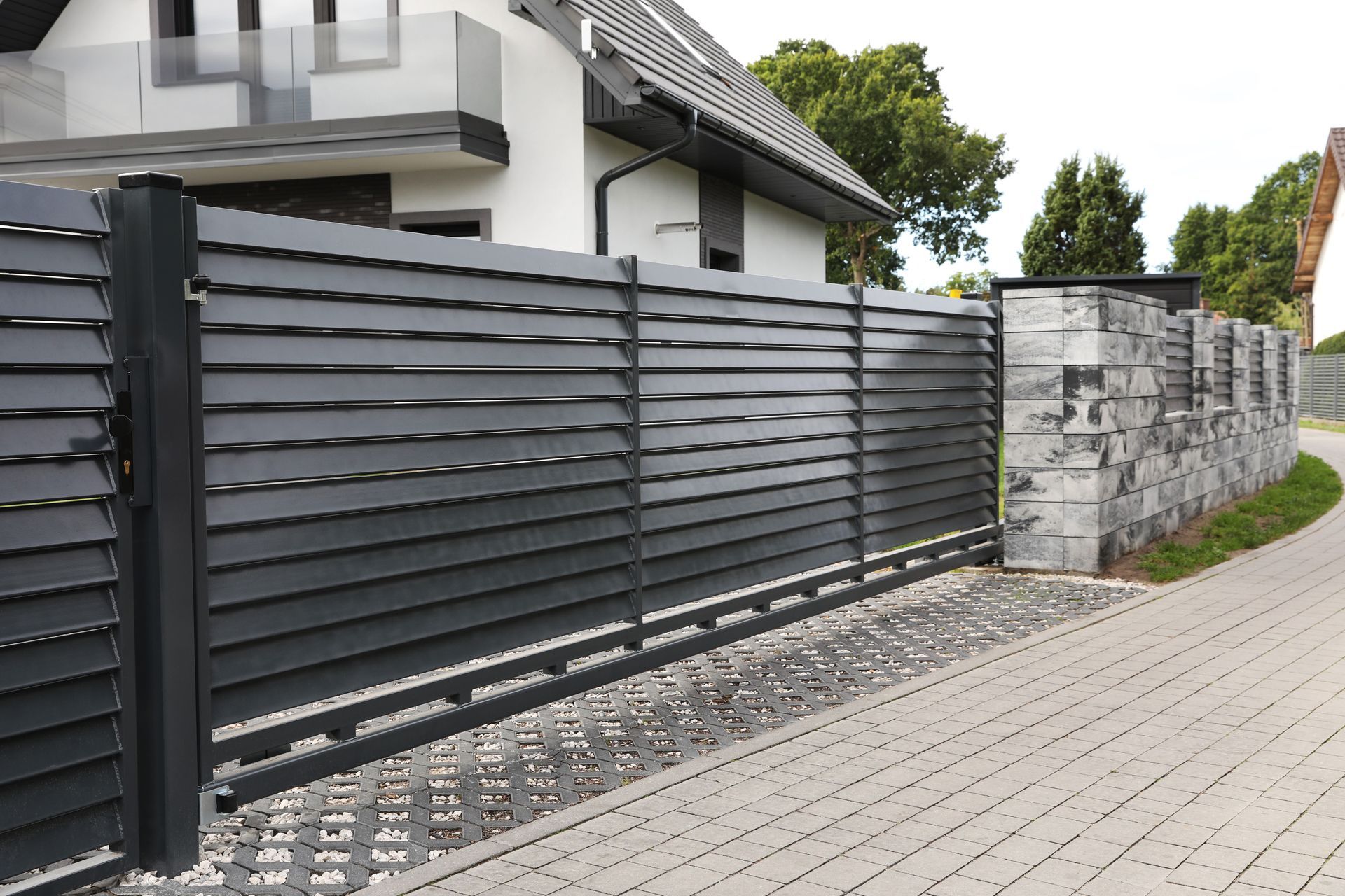 Dark gray horizontal slat fence with gate, light gray block wall, and paved walkway.