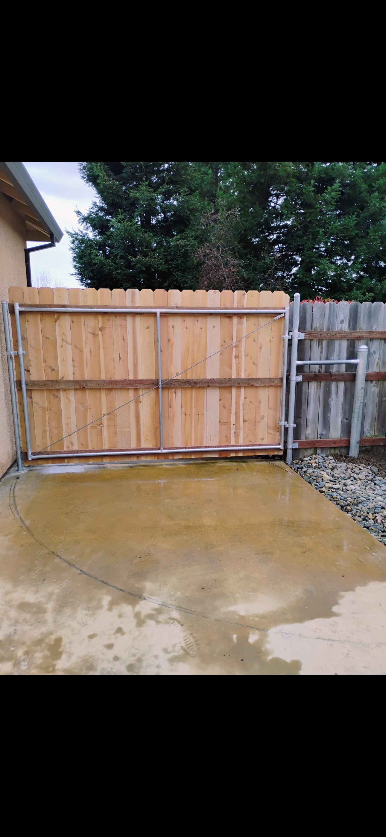 Wooden fence and gate with concrete surface, trees visible in the background.