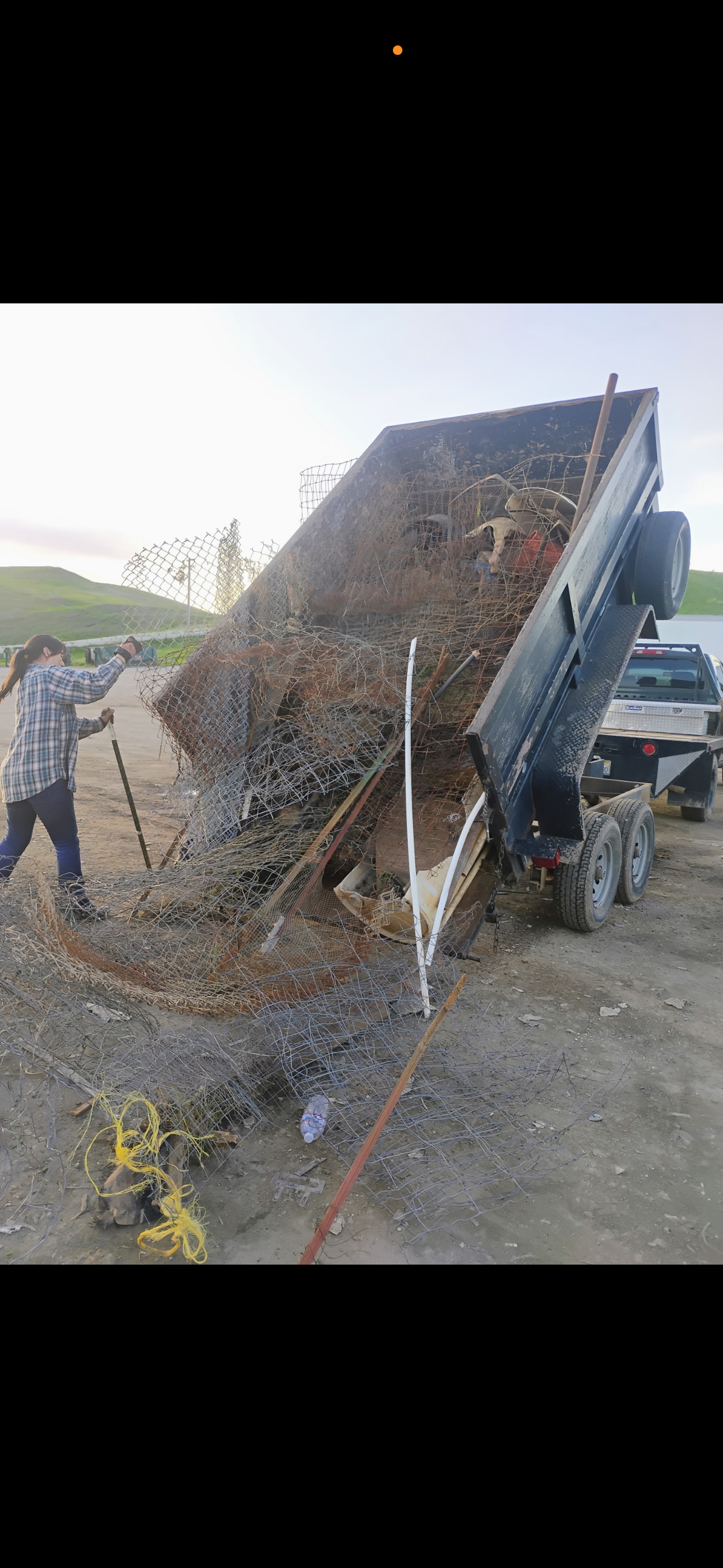 Stone walls frame a driveway leading to a closed black gate. Green lawn and a tree are visible.