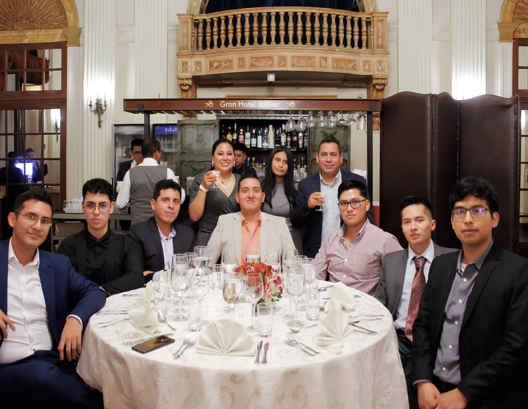 Grupo de personas alrededor de una mesa en un restaurante. Sonriendo, algunos con copas, con atuendo formal.