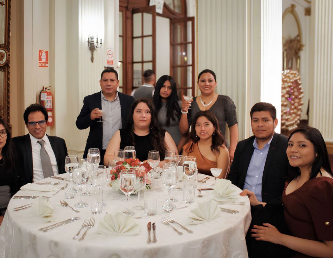 Grupo de personas en una cena formal, sentados alrededor de una mesa en una habitación bien iluminada.