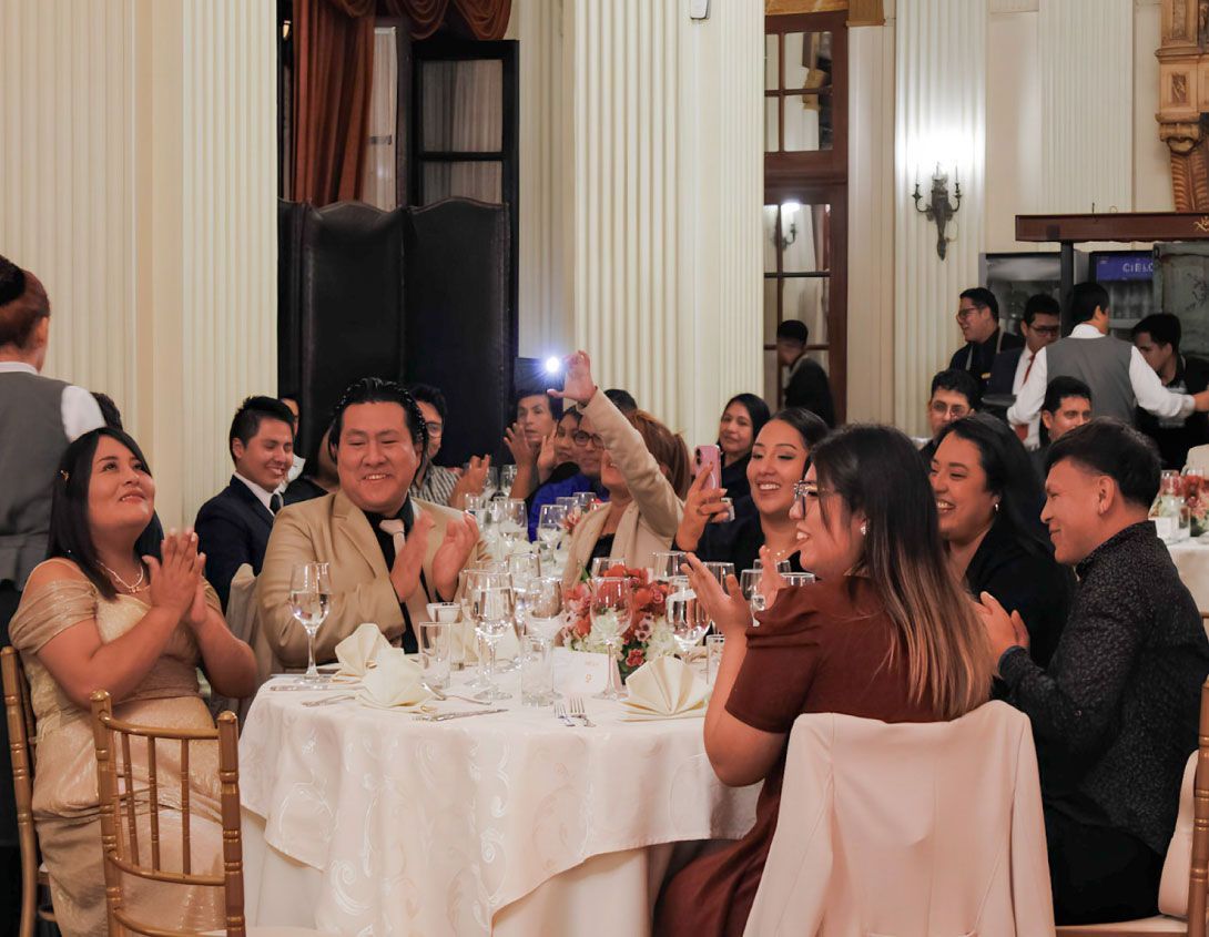 Invitados a un evento formal aplaudiendo, sonriendo y celebrando en una mesa decorada en el interior.