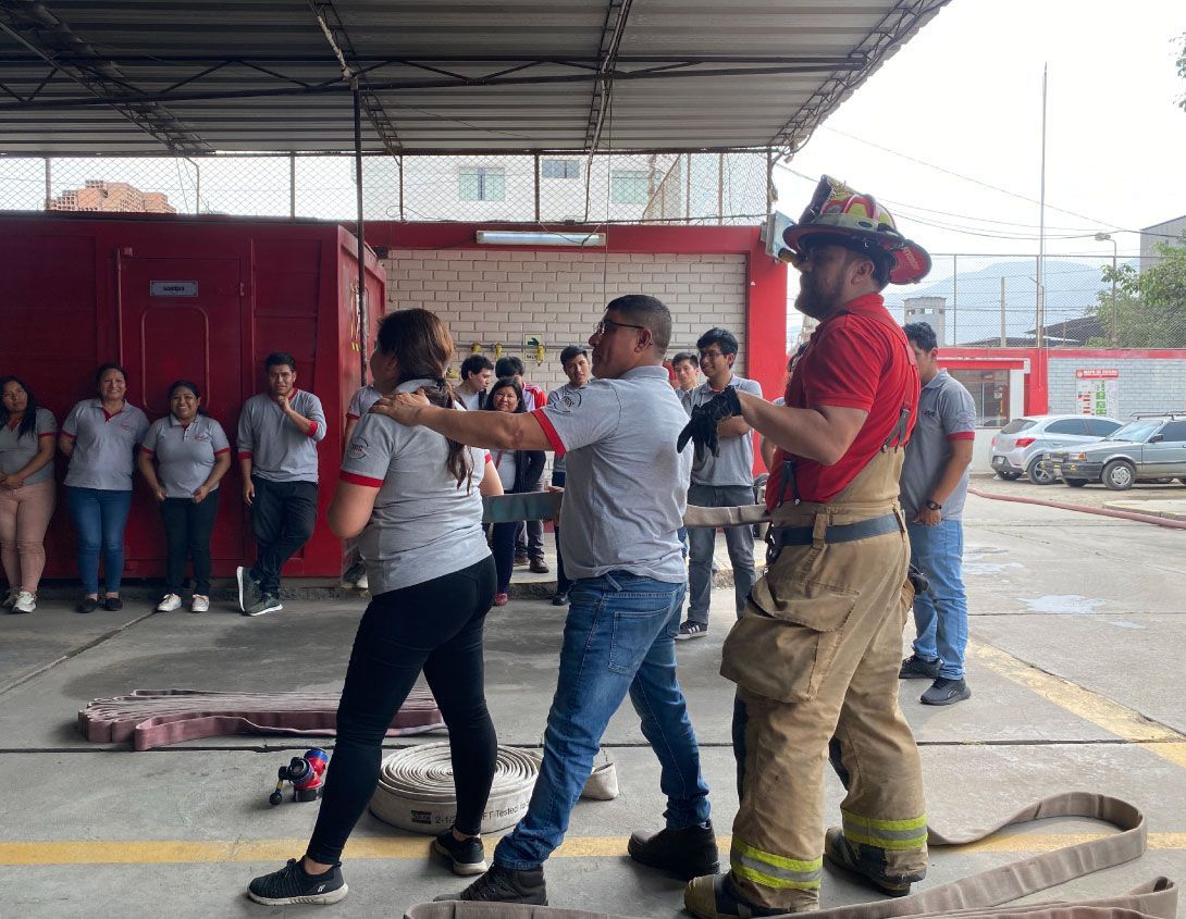 Un bombero demuestra una técnica de rescate con una mujer, mientras otros observan.