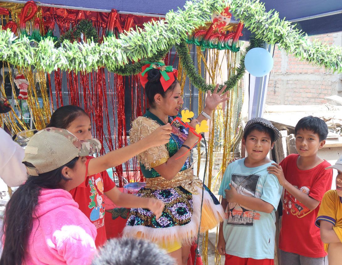 Los niños miran a un artista con una flor, globos y decoraciones navideñas en un evento al aire libre.