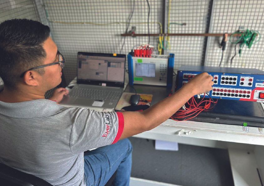 Hombre con gafas trabajando con equipos de pruebas electrónicos, dentro de una habitación pequeña.