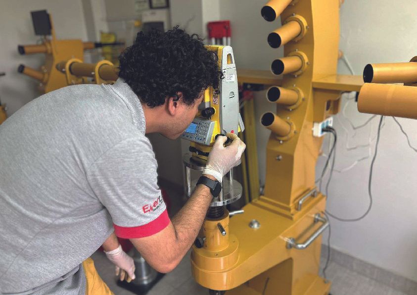 Un hombre con camisa gris y guantes examina una máquina industrial amarilla en el interior.