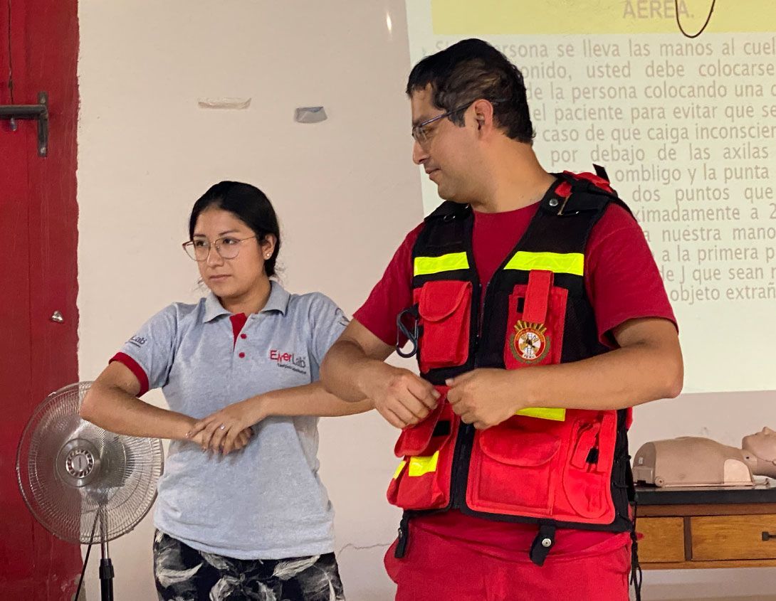 Dos personas demuestran un procedimiento de primeros auxilios en un espacio cerrado. 