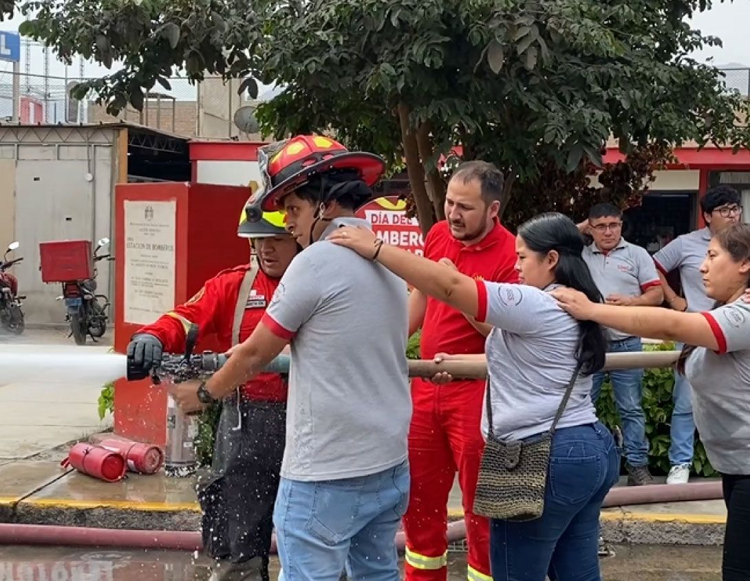 Bomberos demuestran el uso de mangueras contra incendios con civiles al aire libre.