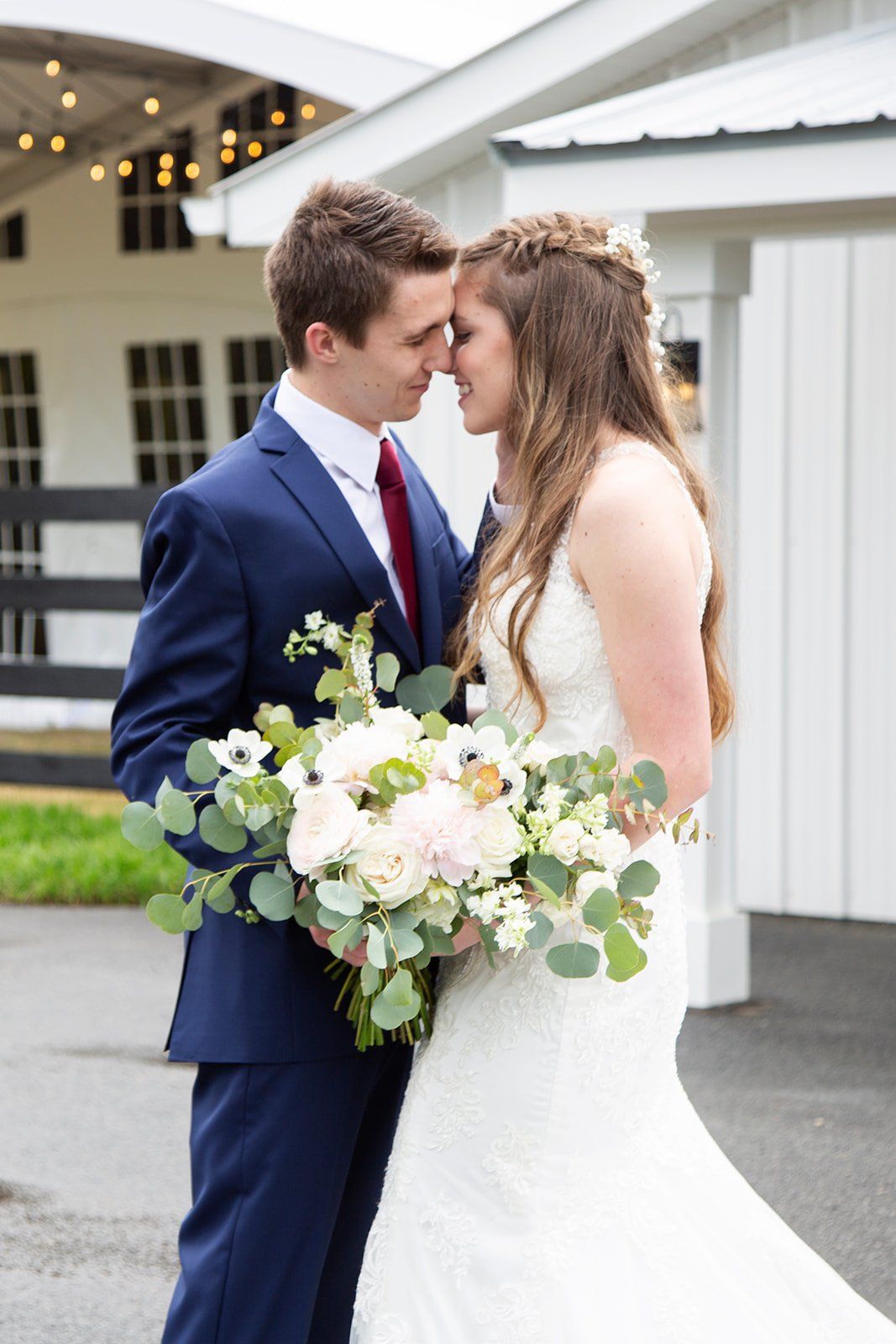 A bride and groom are kissing in front of a white barn.