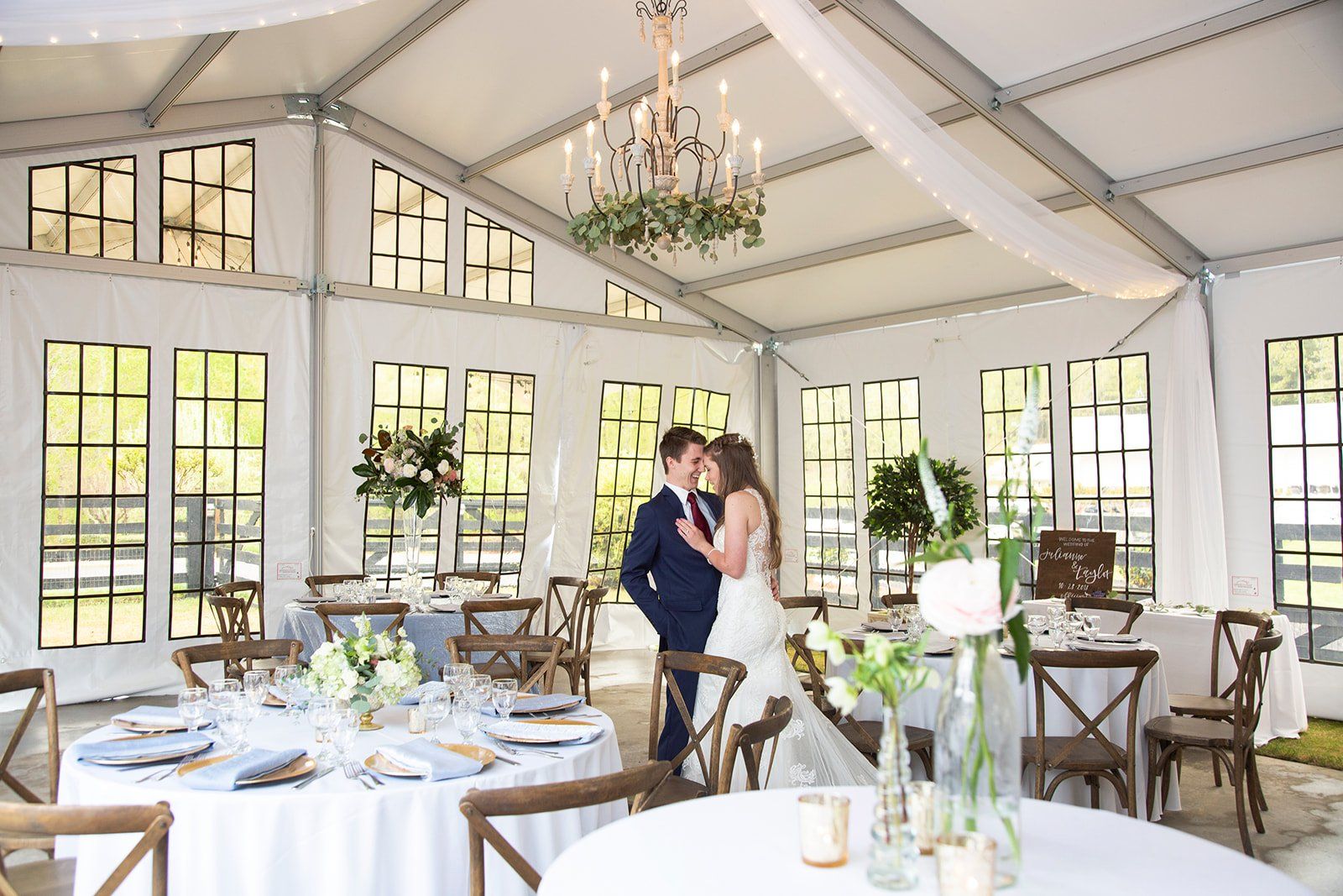 A bride and groom are standing in a tent surrounded by tables and chairs.