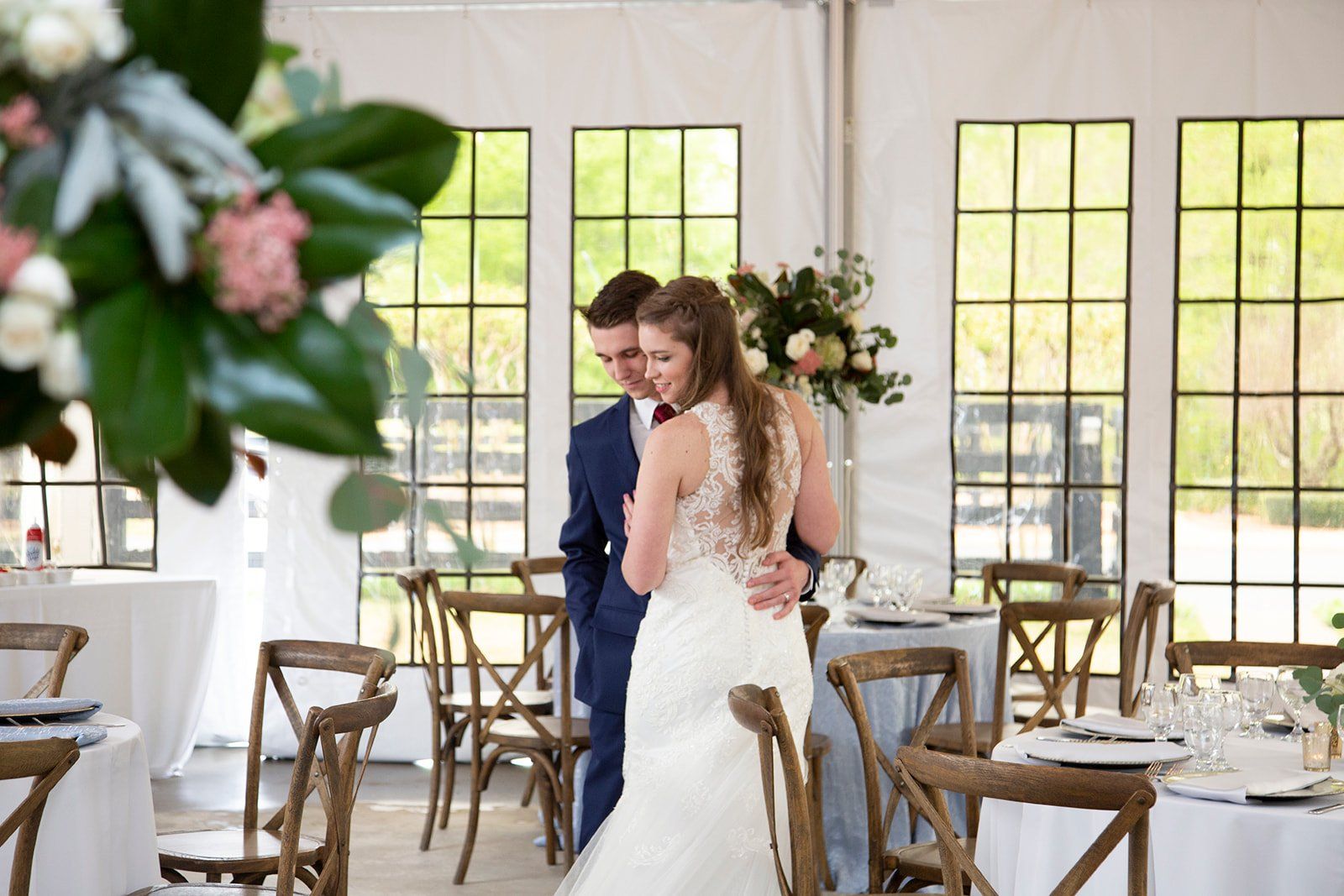 A bride and groom are standing in a room with tables and chairs.