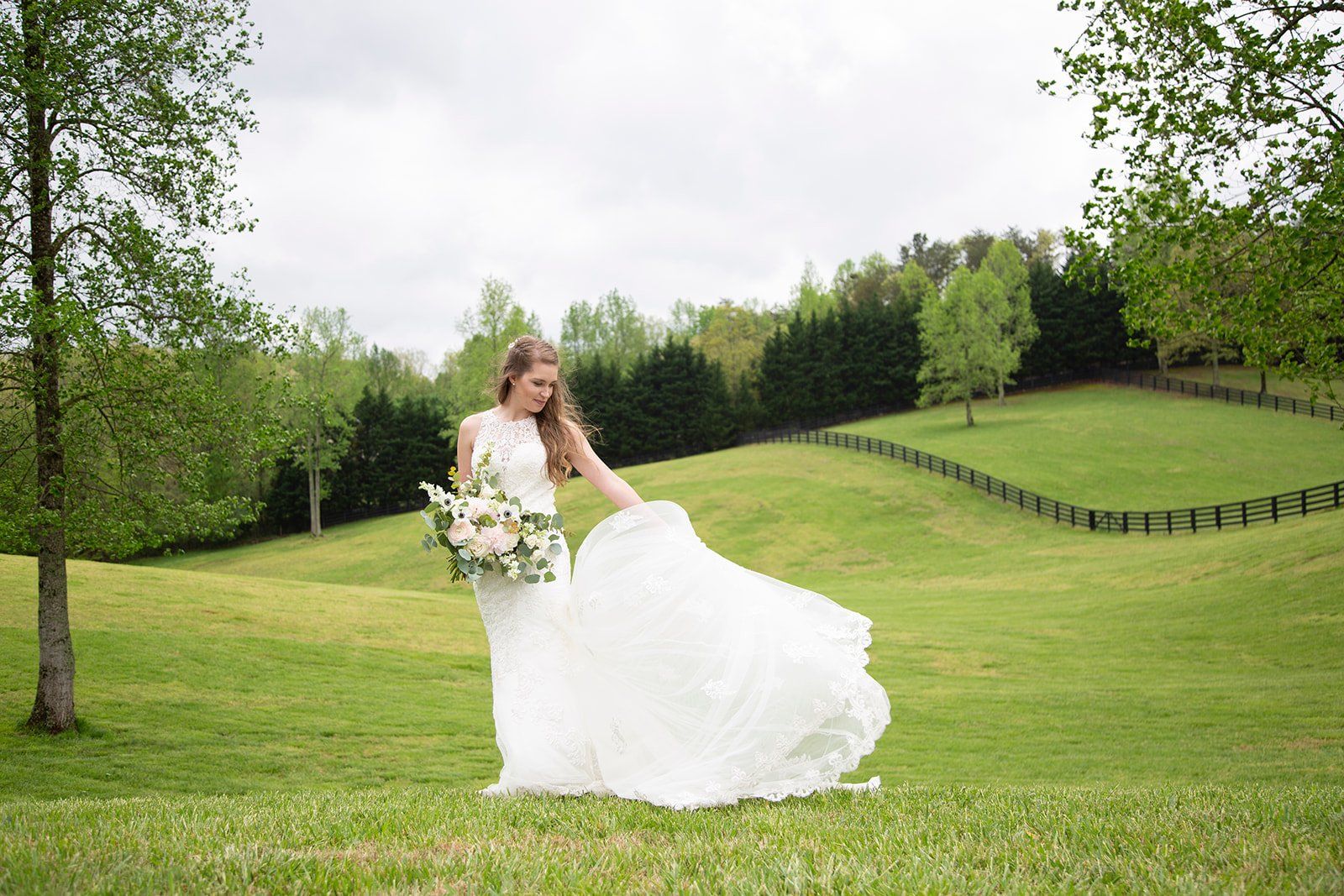 A bride in a wedding dress is standing in a grassy field holding a bouquet of flowers.