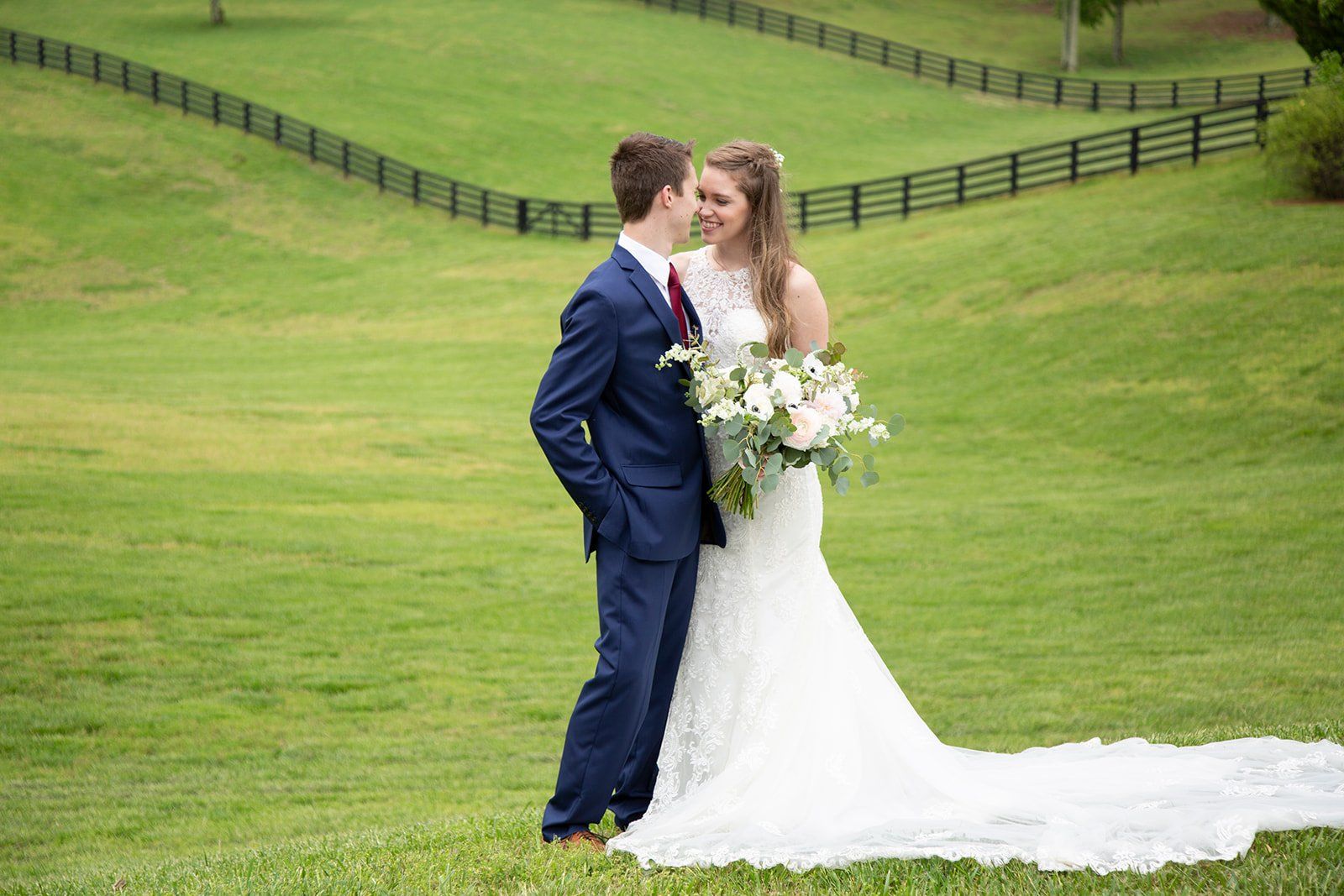 A bride and groom are kissing in a grassy field.