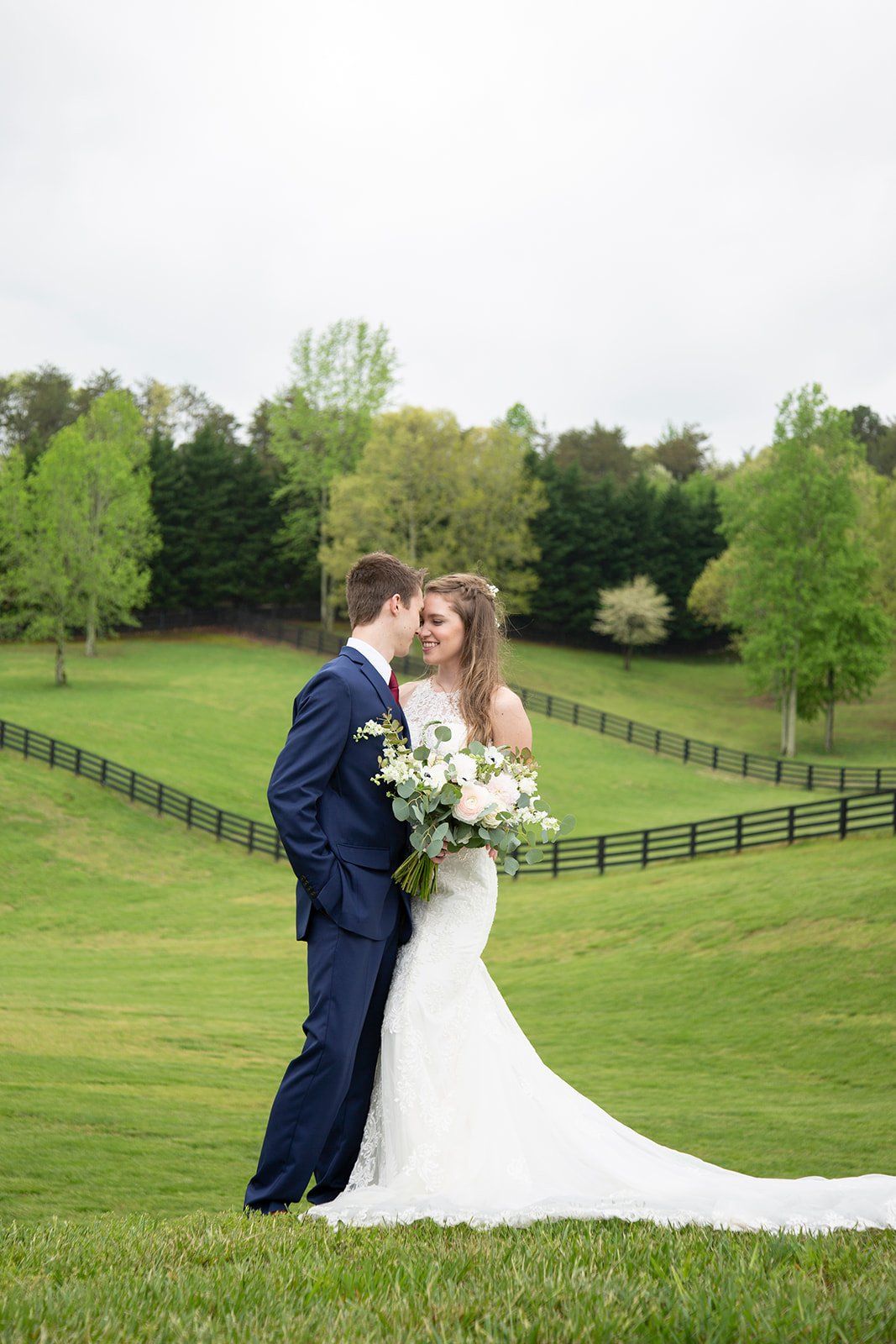 A bride and groom are posing for a picture in a grassy field.